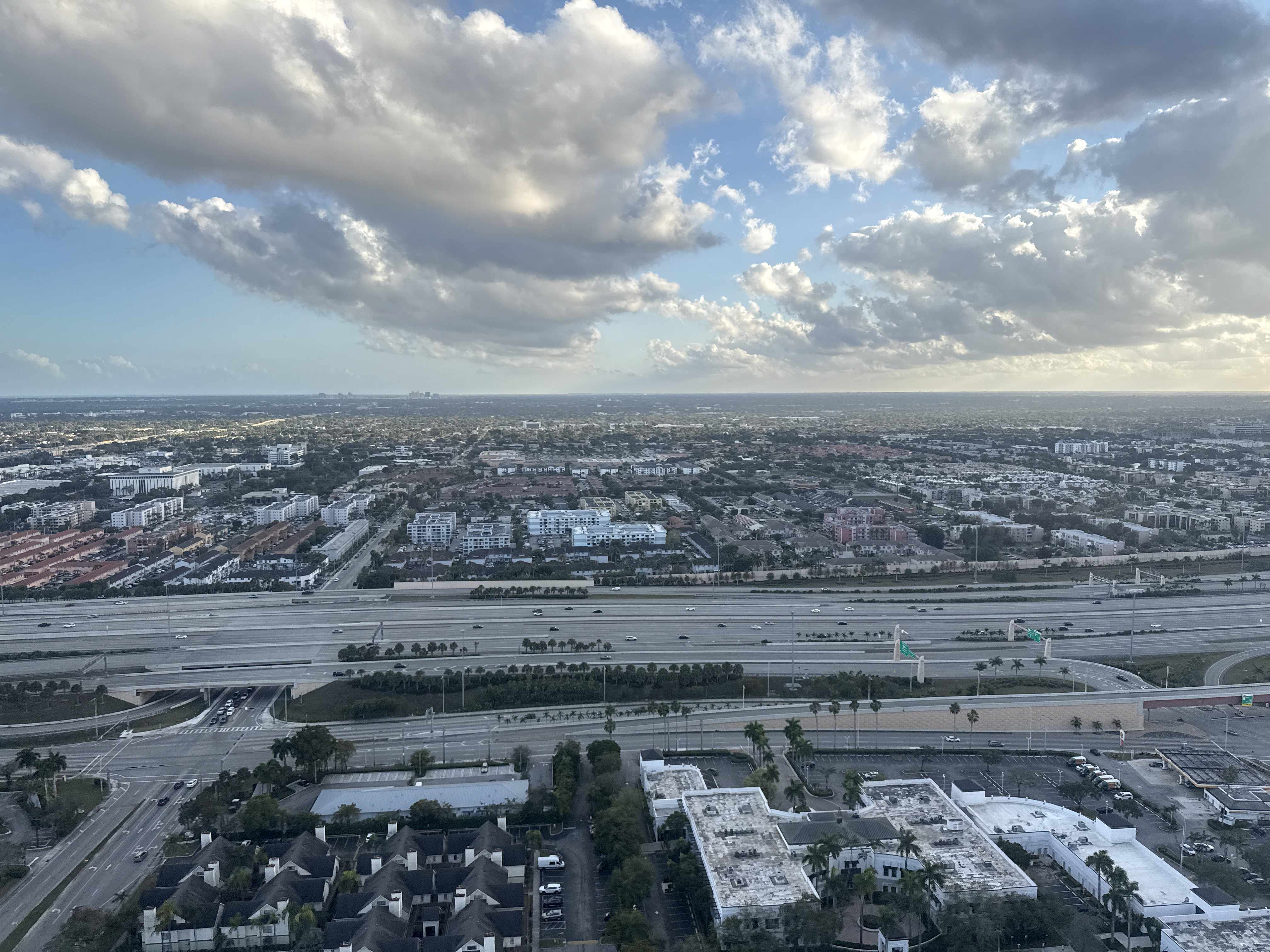 Pohled z výšky na město, dálnici a mraky nad obzorem.