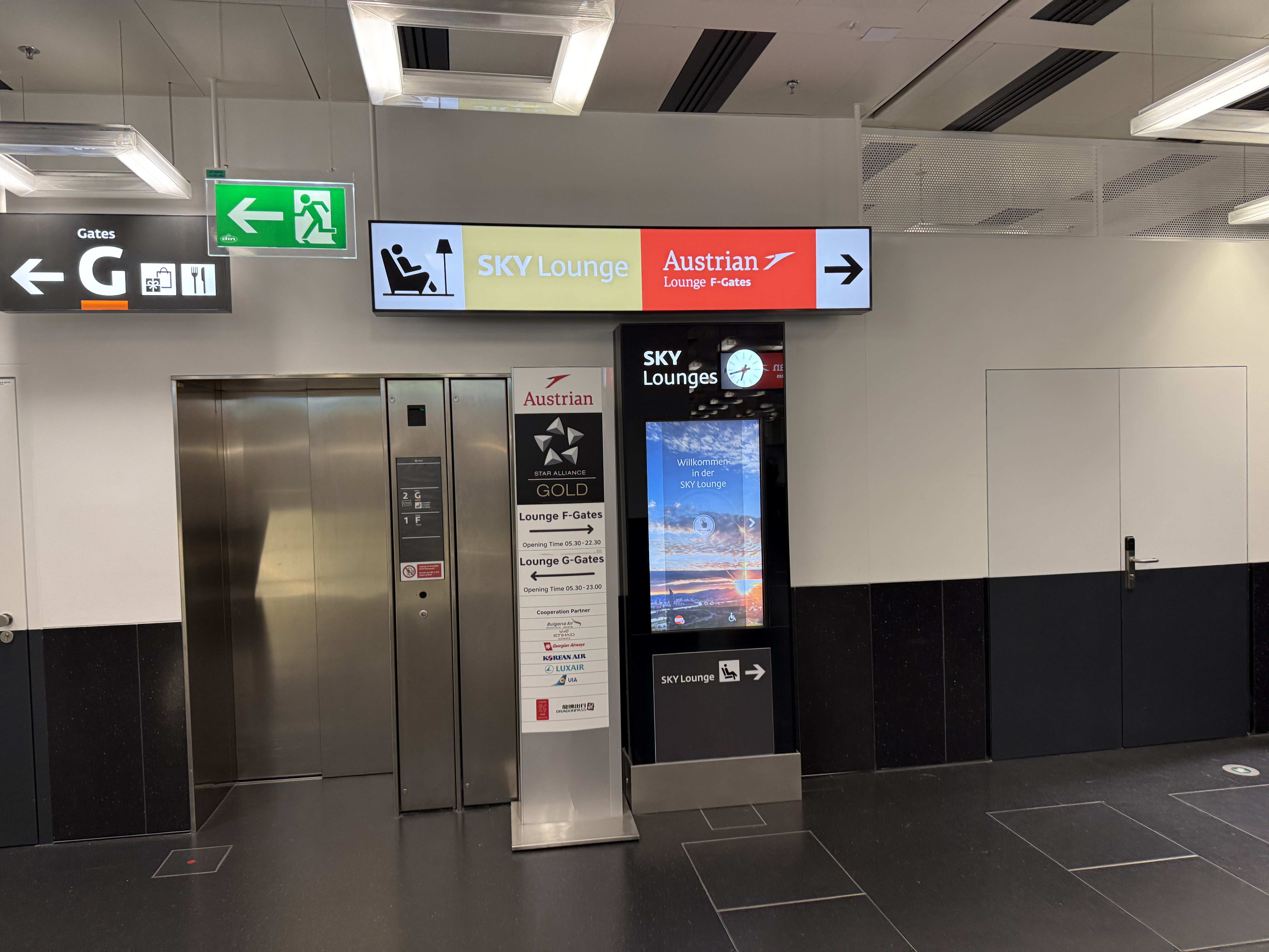 Navigační cedule SKY Lounge, Austrian Lounge F-Gates, směrovka; vedle výtah a kiosk