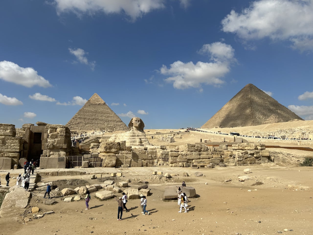 Pyramidy v Gíze se Sfingou, turisty a modrou oblohou s mraky