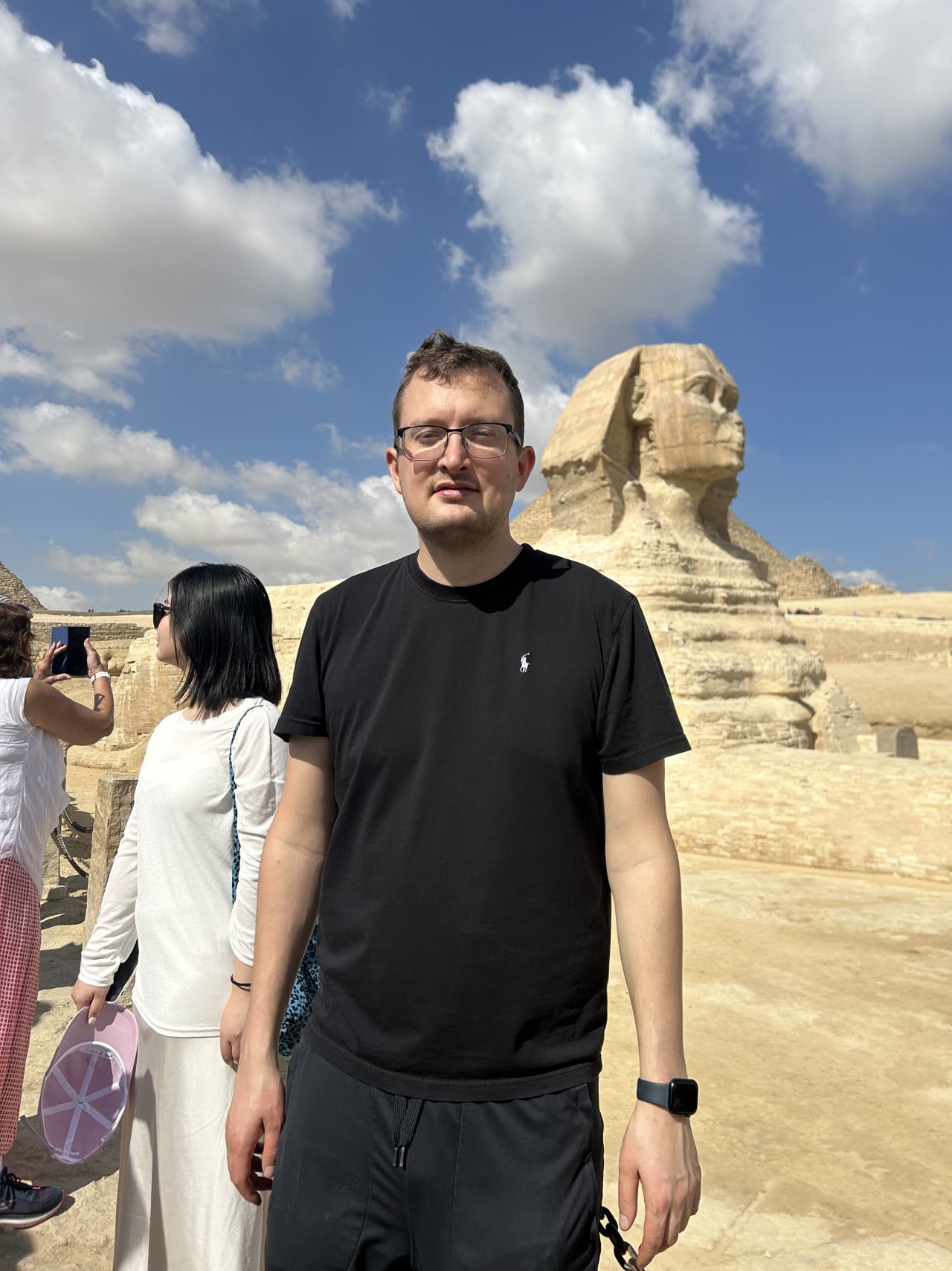 Muž před Velkou sfingou v Gíze, turisté a modrá obloha s mraky