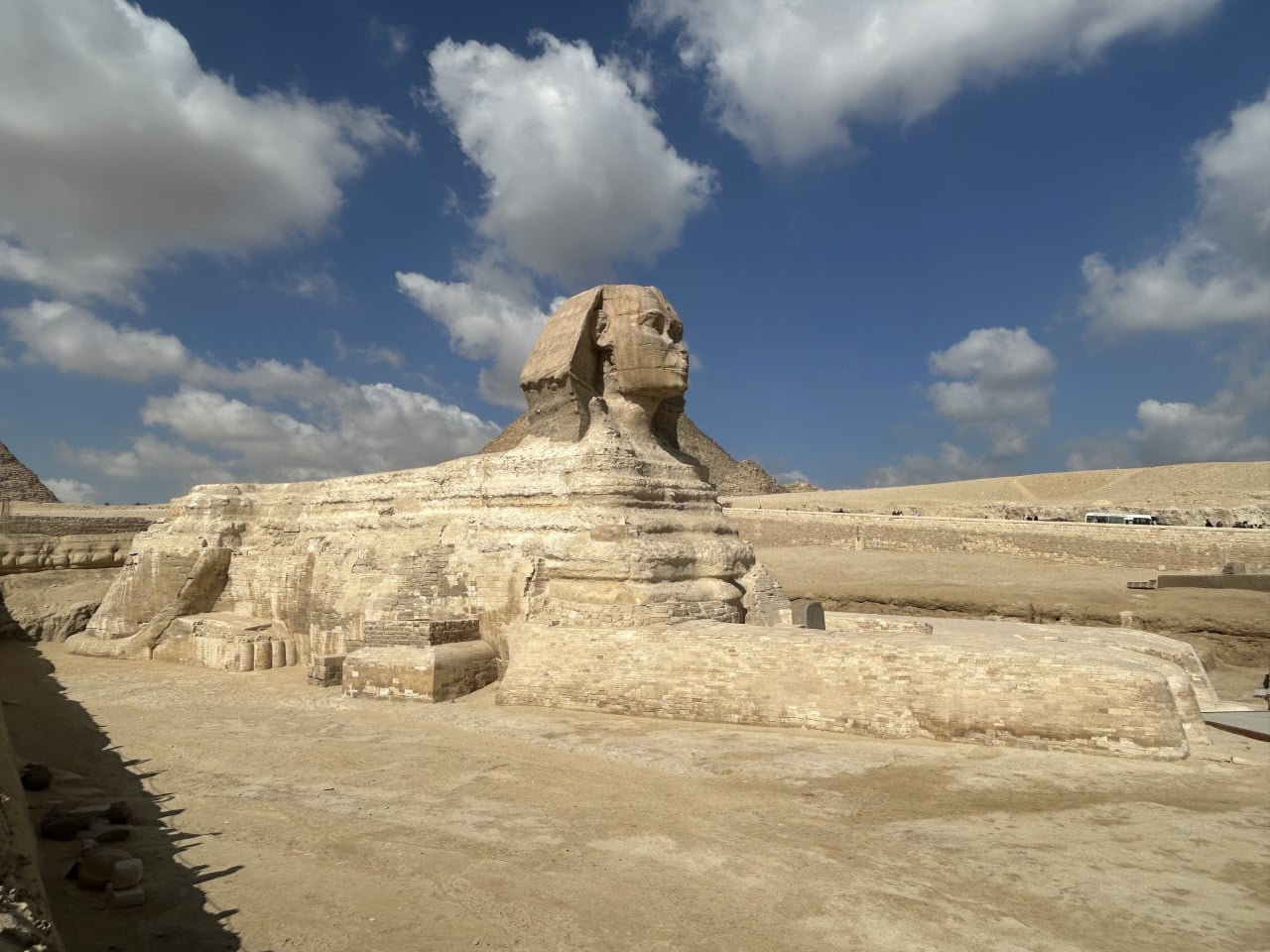 Velká sfinga v Gíze pod modrou oblohou s mraky, pyramidy v pozadí