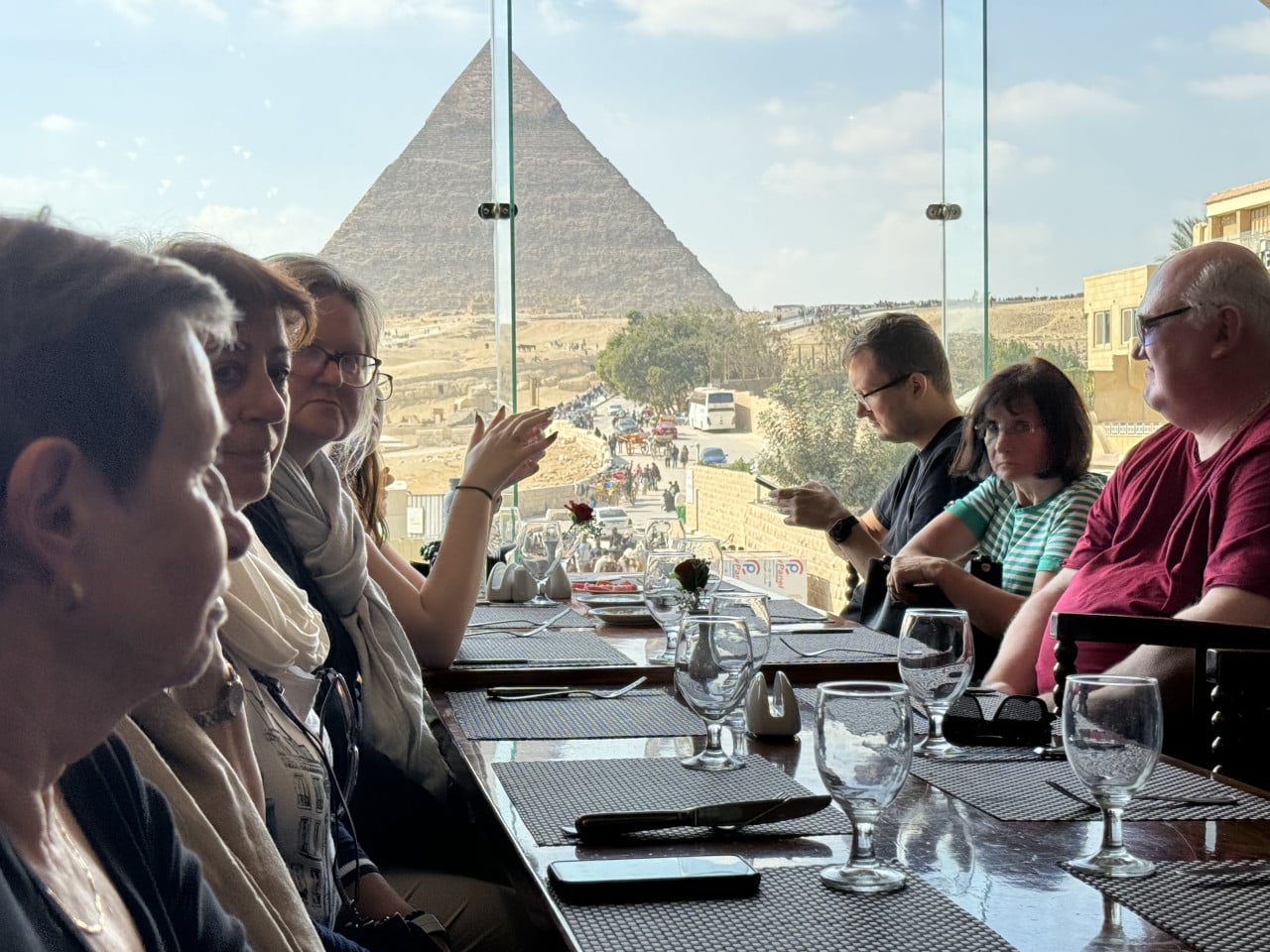 Lidé sedí u stolu v restauraci s výhledem na Cheopsovu pyramidu v Gíze.