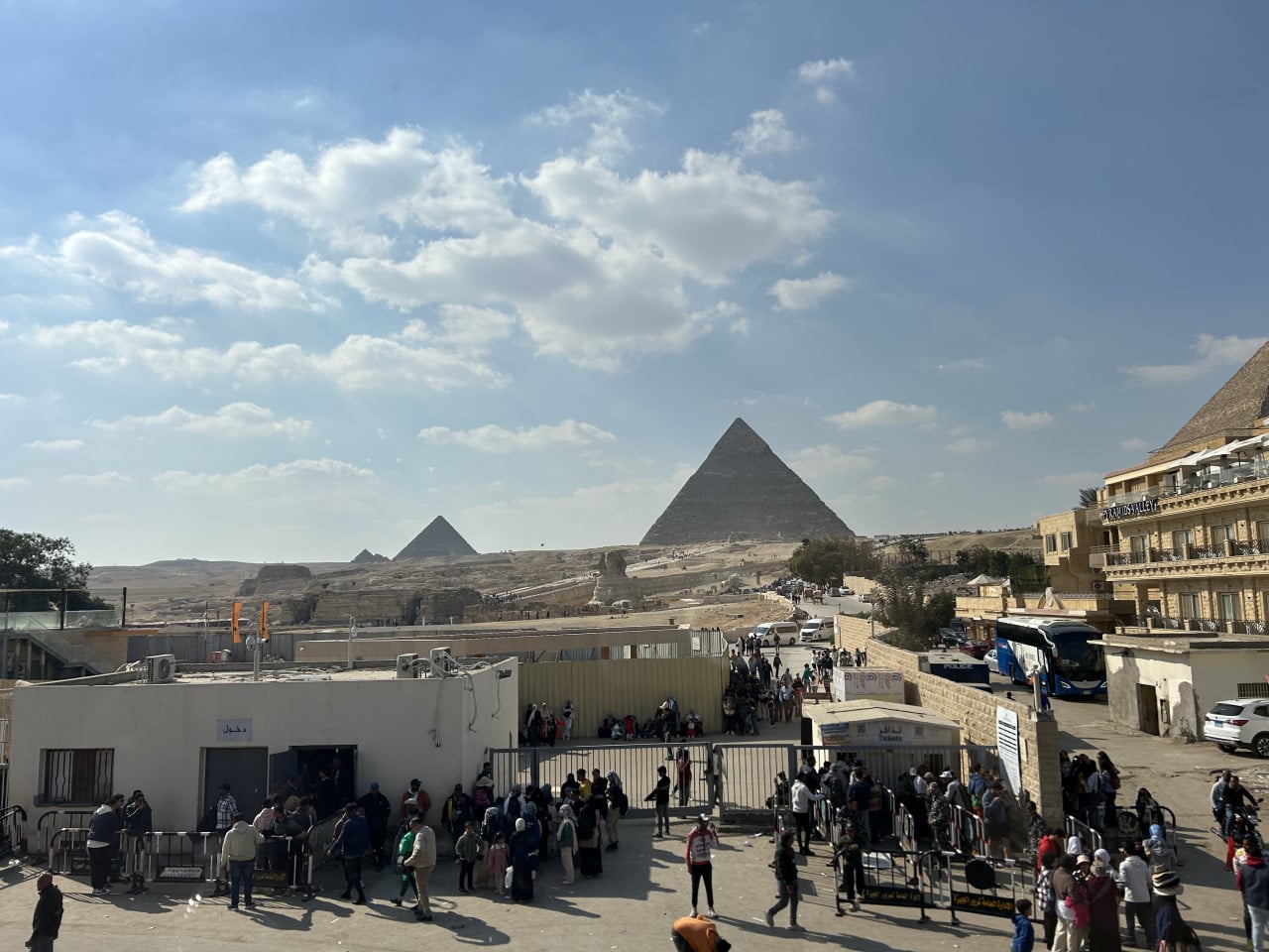Pohled na pyramidy v Gíze, Sfinhu a davy turistů u vstupu.