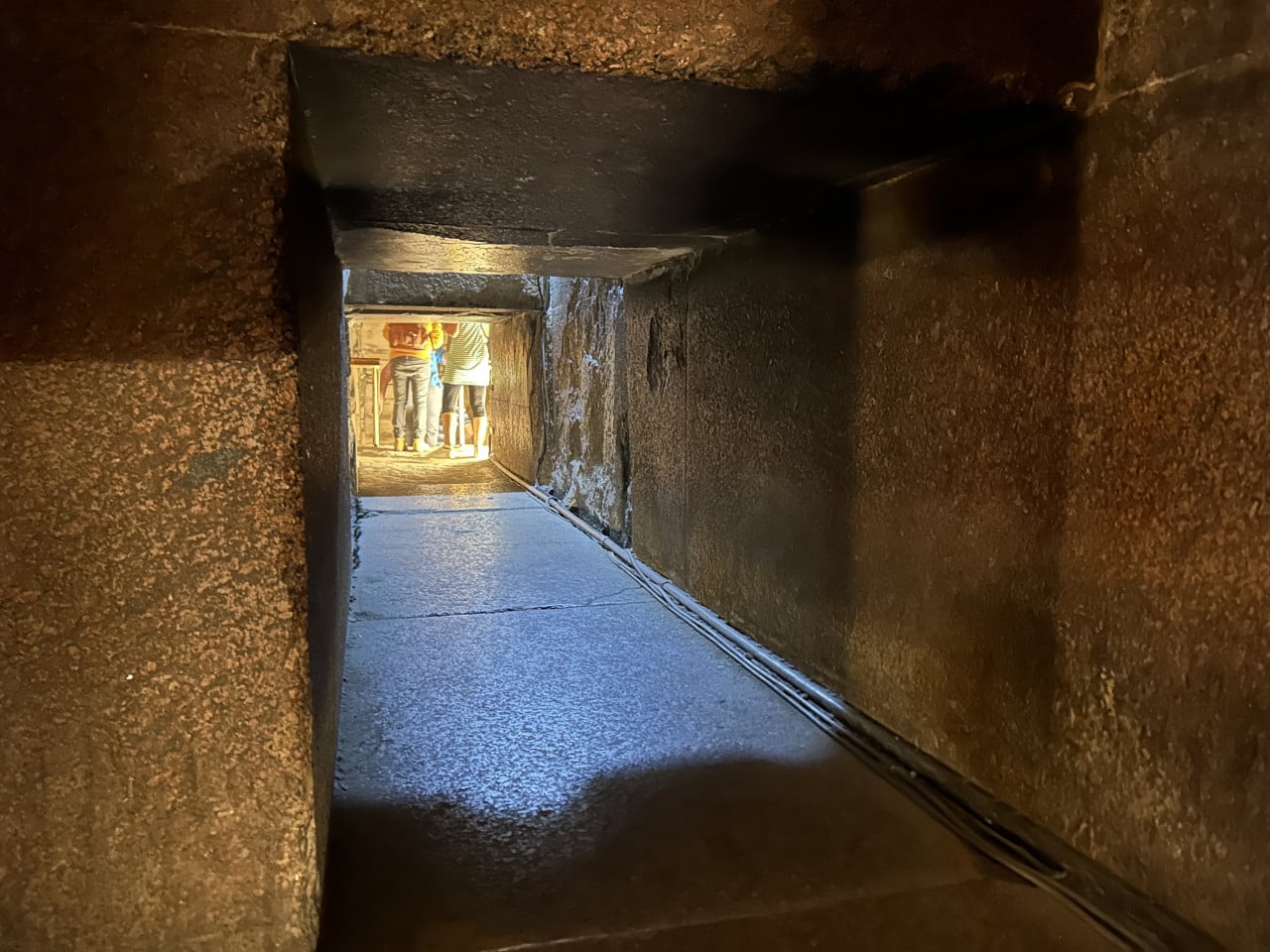 Úzká chodba uvnitř Cheopsovy pyramidy s turisty u osvětleného východu.