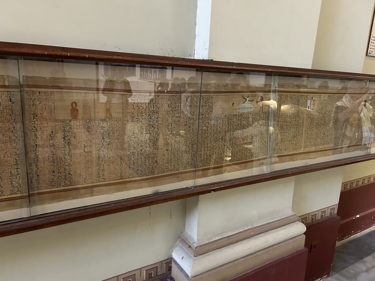 Skleněná vitrína s dlouhým egyptským papyrem popsaným hieroglyfy v muzeu