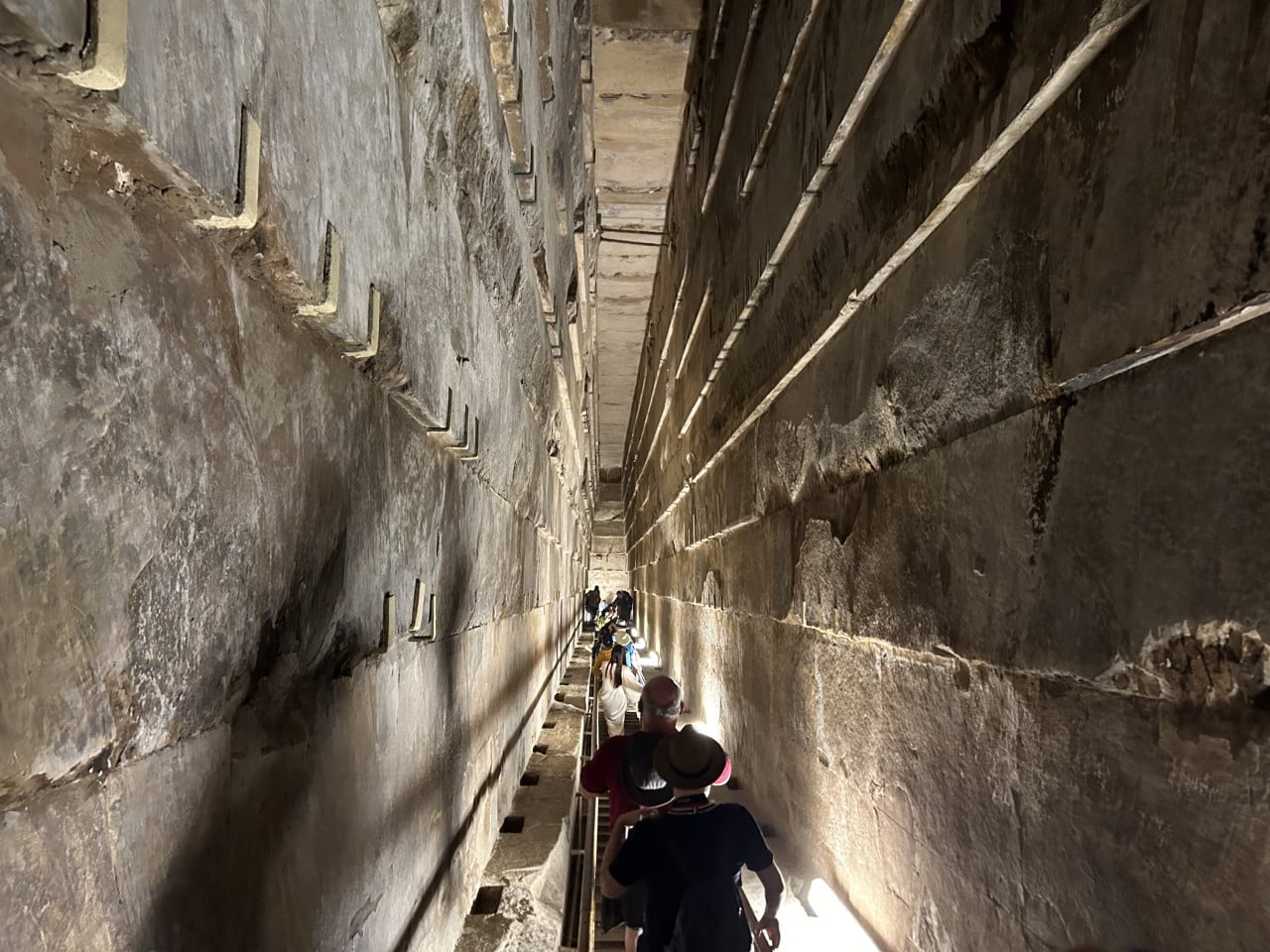 Úzká kamenná chodba uvnitř pyramidy s návštěvníky sestupujícími po schodech.