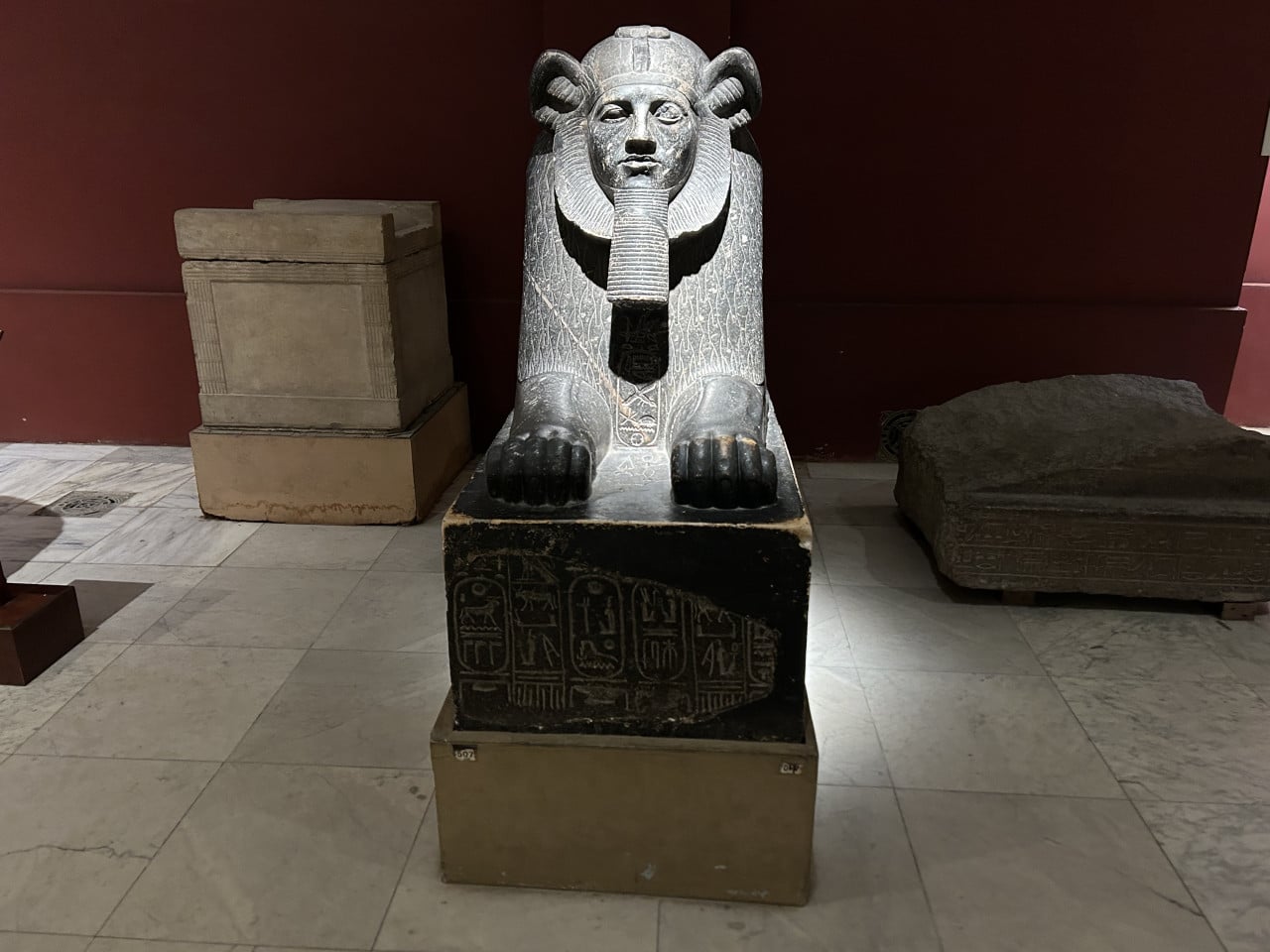 Sarkofág s podobou sfingy v egyptském muzeu, obklopený kamennými bloky a deskami