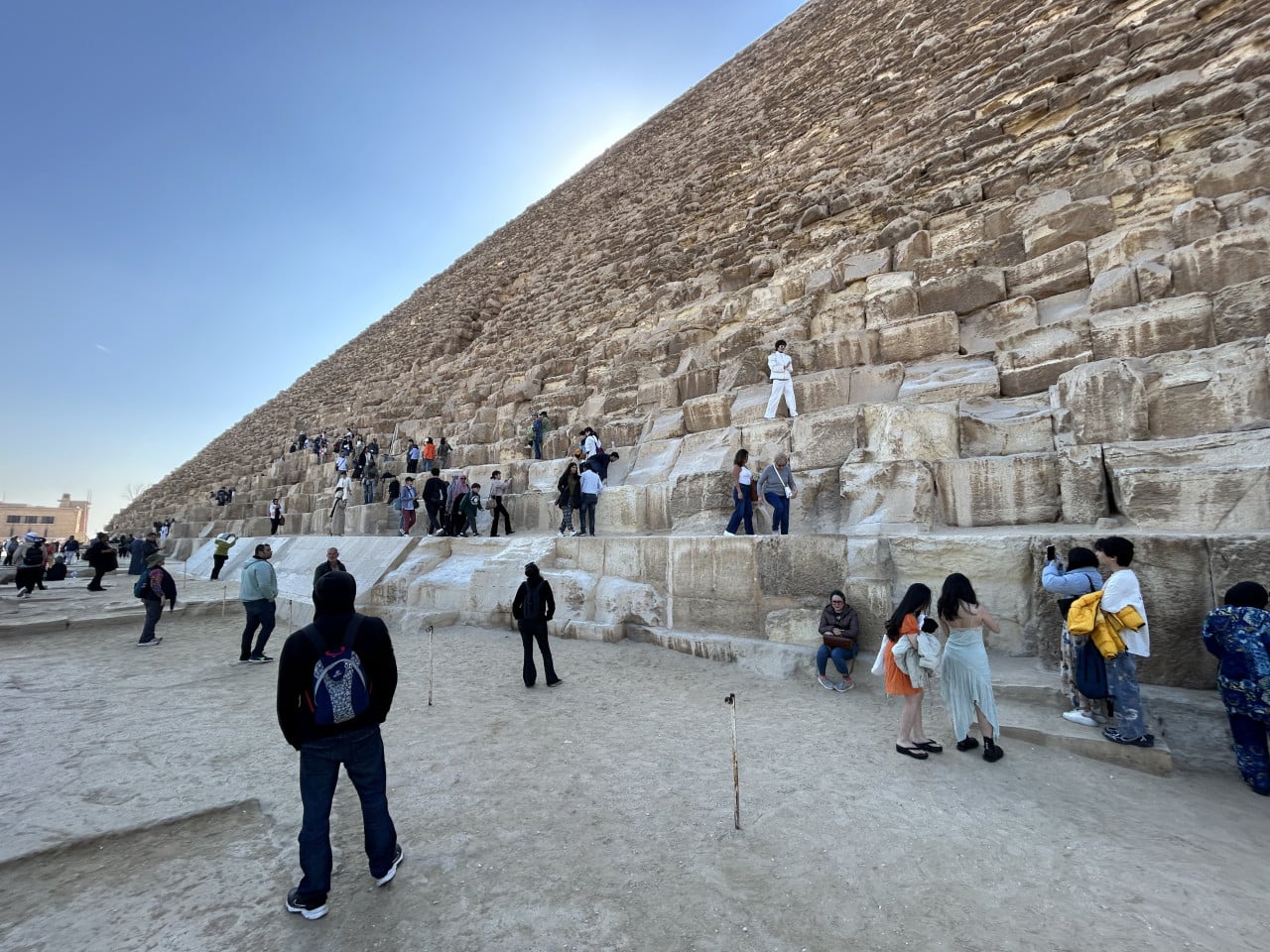 Turisté u paty Cheopsovy pyramidy v Gíze pod modrou oblohou