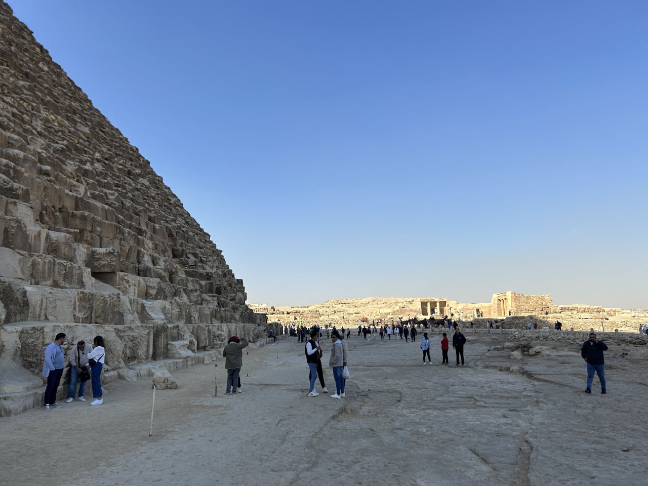 Pod úpatím Cheopsovy pyramidy turisté stojí na kamenné plošině v Gíze.