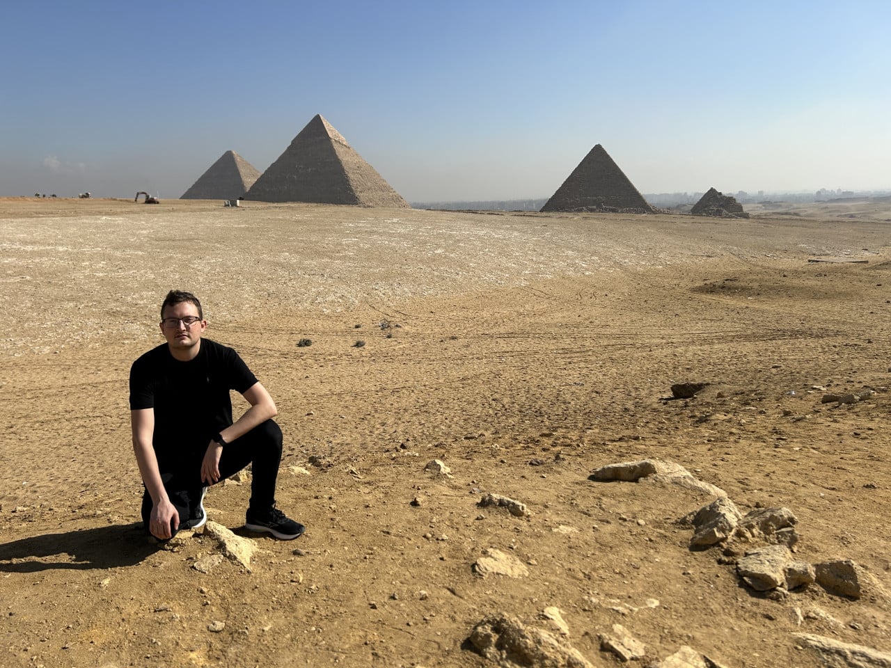 Muž klečí v poušti před pyramidami v Gíze za jasného dne
