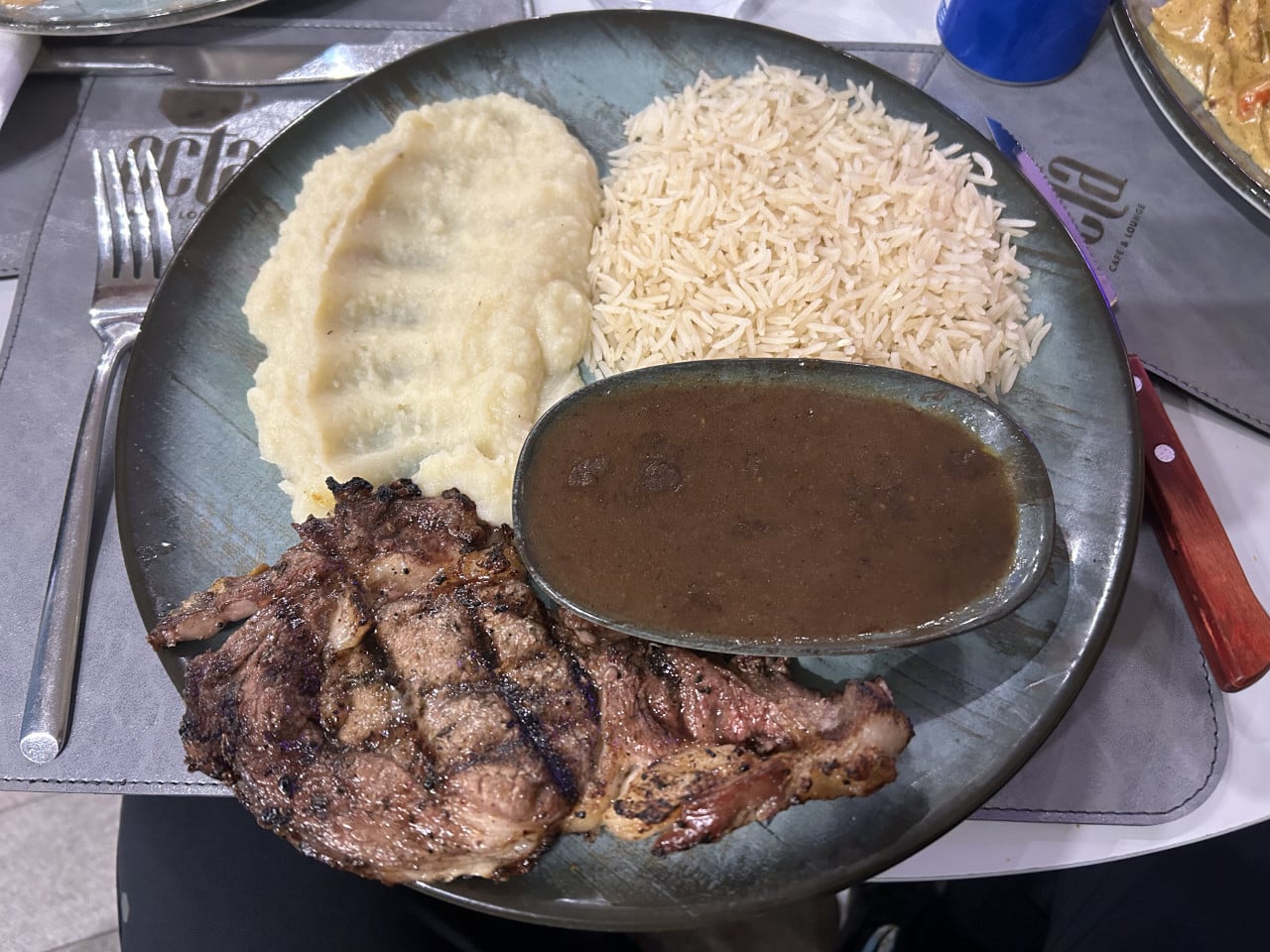 Talíř s grilovaným masem, rýží, kaší a tmavou omáčkou v restauraci.