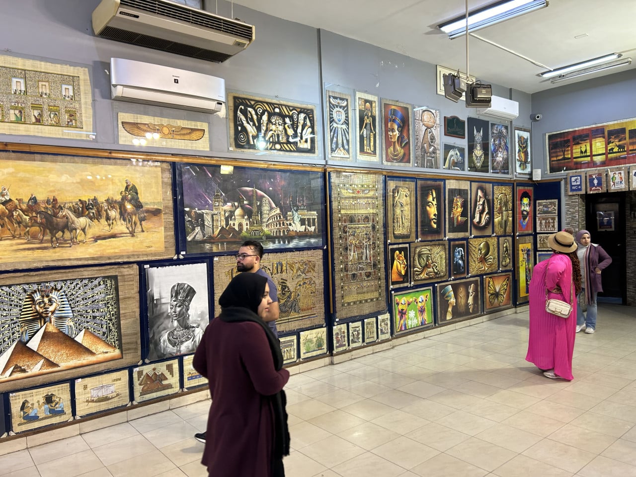 Obchod se suvenýry s egyptskými obrazy, lidé prohlížejí nástěnky a plakáty