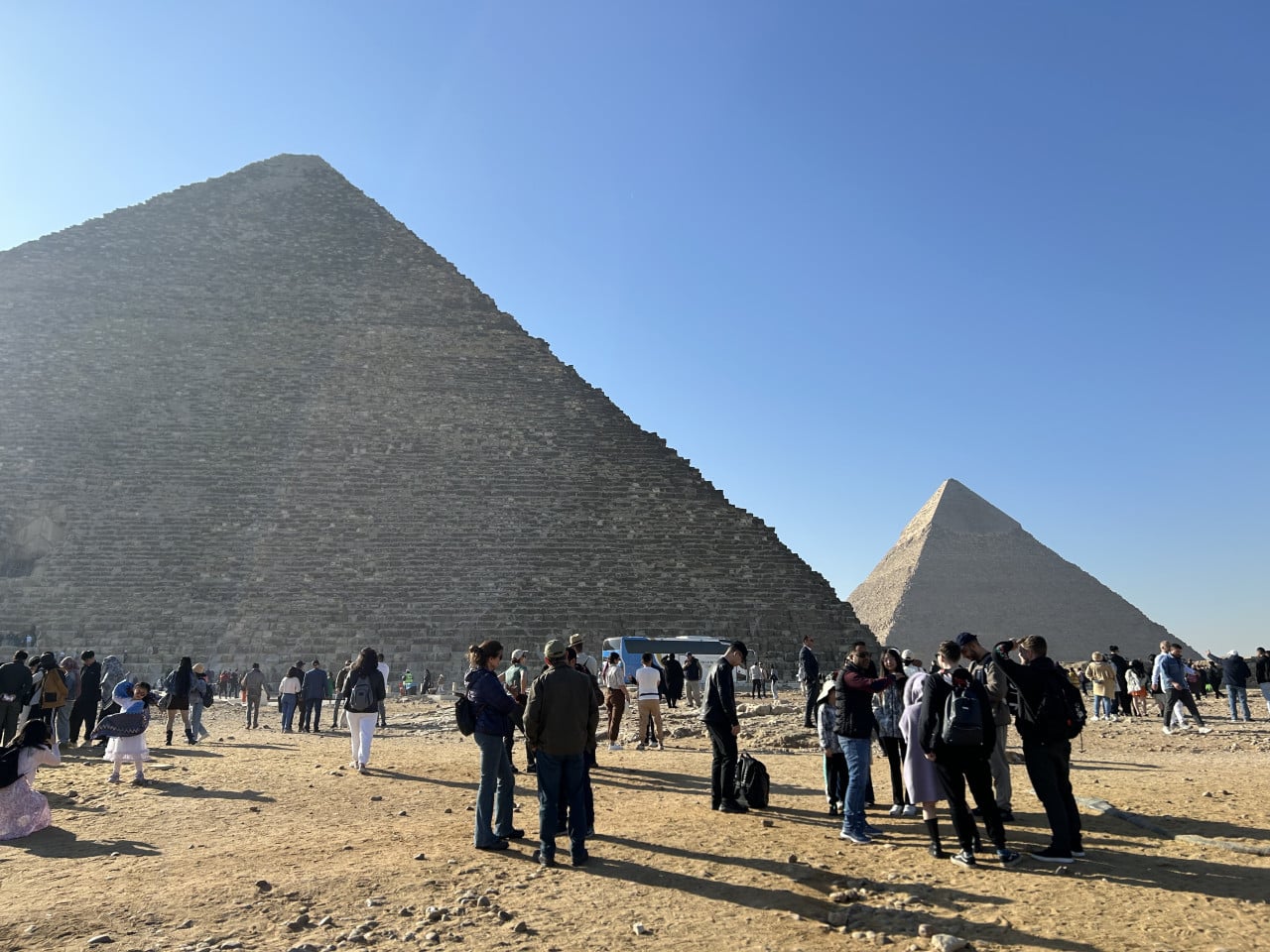 Pyramidy v Gíze s turisty pod modrou oblohou, Cheopsova pyramida vlevo v popředí