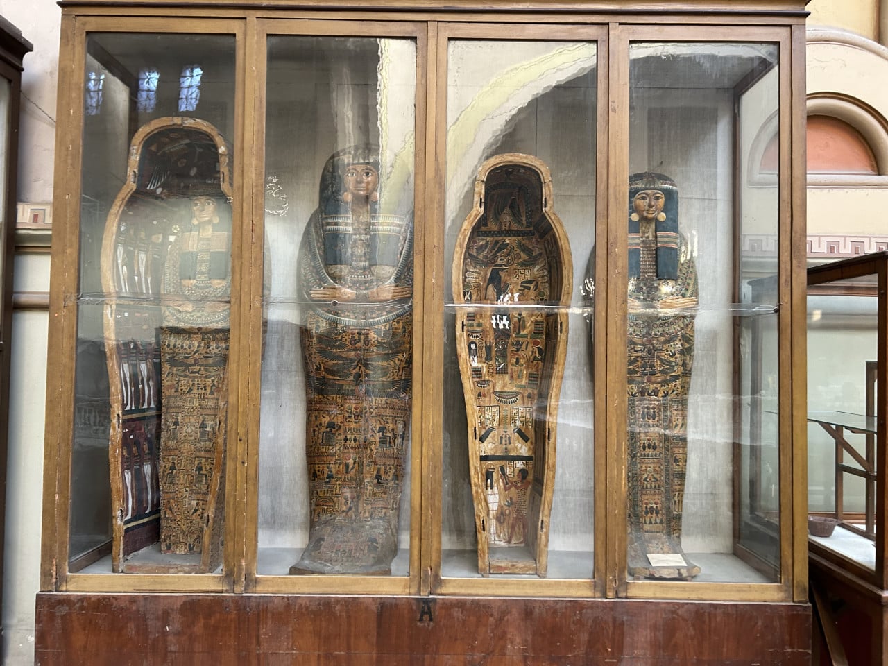 Čtyři zdobené egyptské sarkofágy ve skleněné vitríně v muzeu