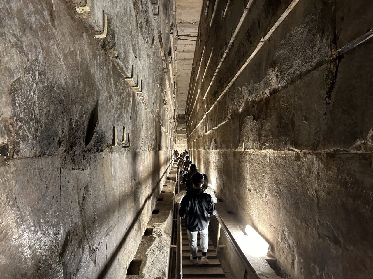 Úzká kamenná chodba uvnitř pyramidy s turisty na schodech.