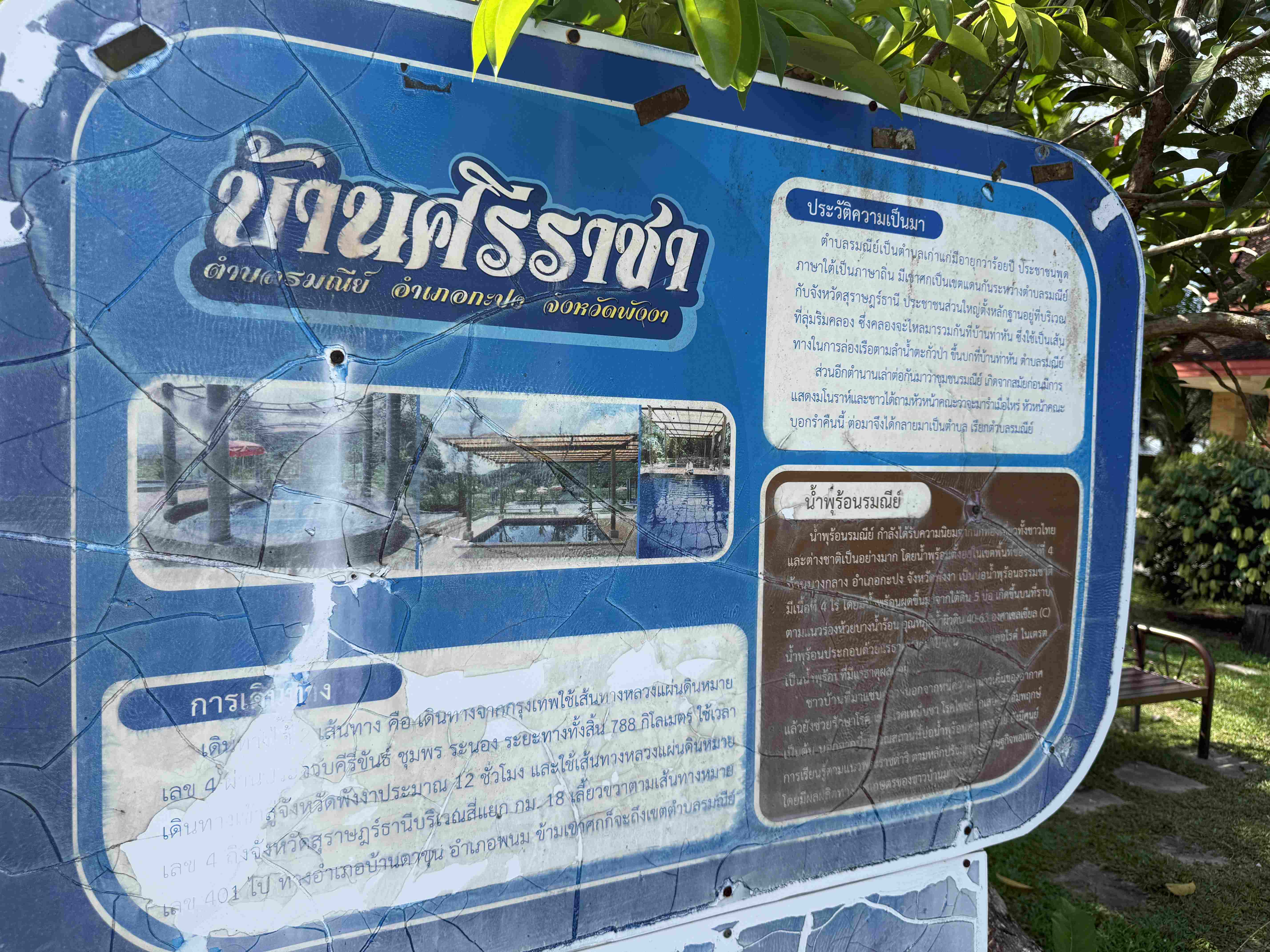 Popraskaná modrá informační tabule v thajštině บ้านร่มณี s fotkami lázní.