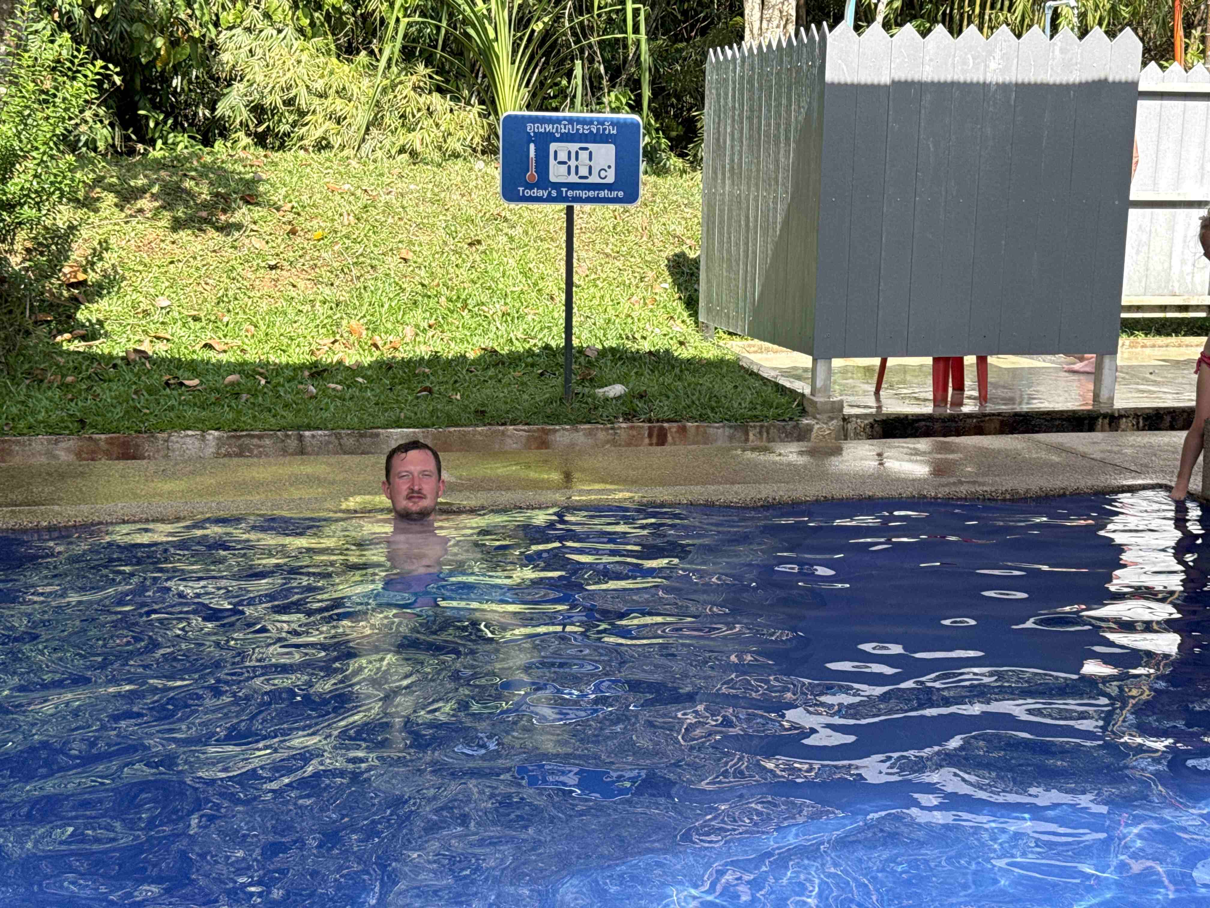 Muž v bazénu, cedule Today's Temperature 38°C u Rommanee Hot Spring