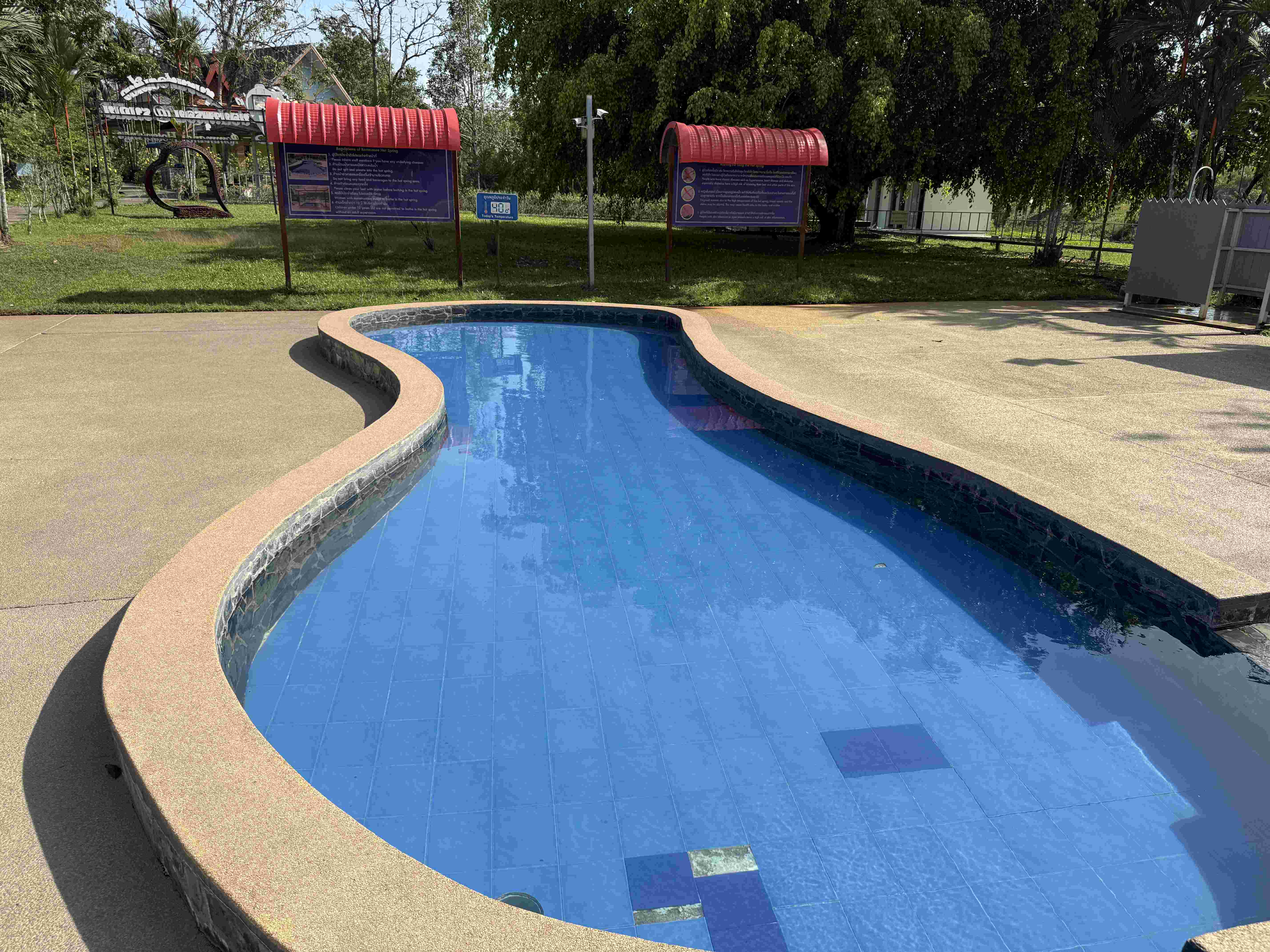Malý modře kachličkovaný bazének s oblými okraji, informační tabule a stromy v pozadí