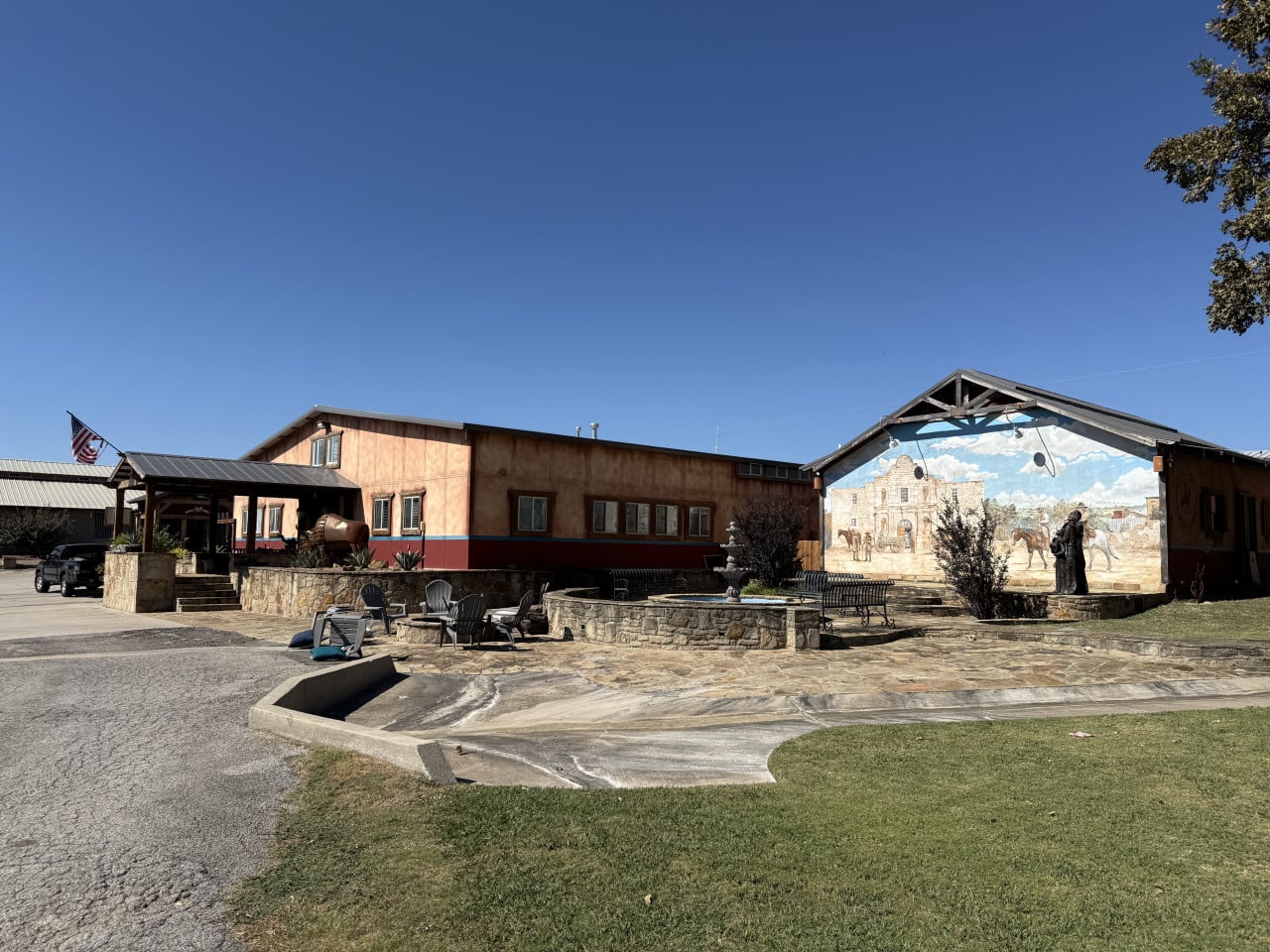 Ranch s budovami, muralem s koňmi a venkovním posezením pod modrou oblohou