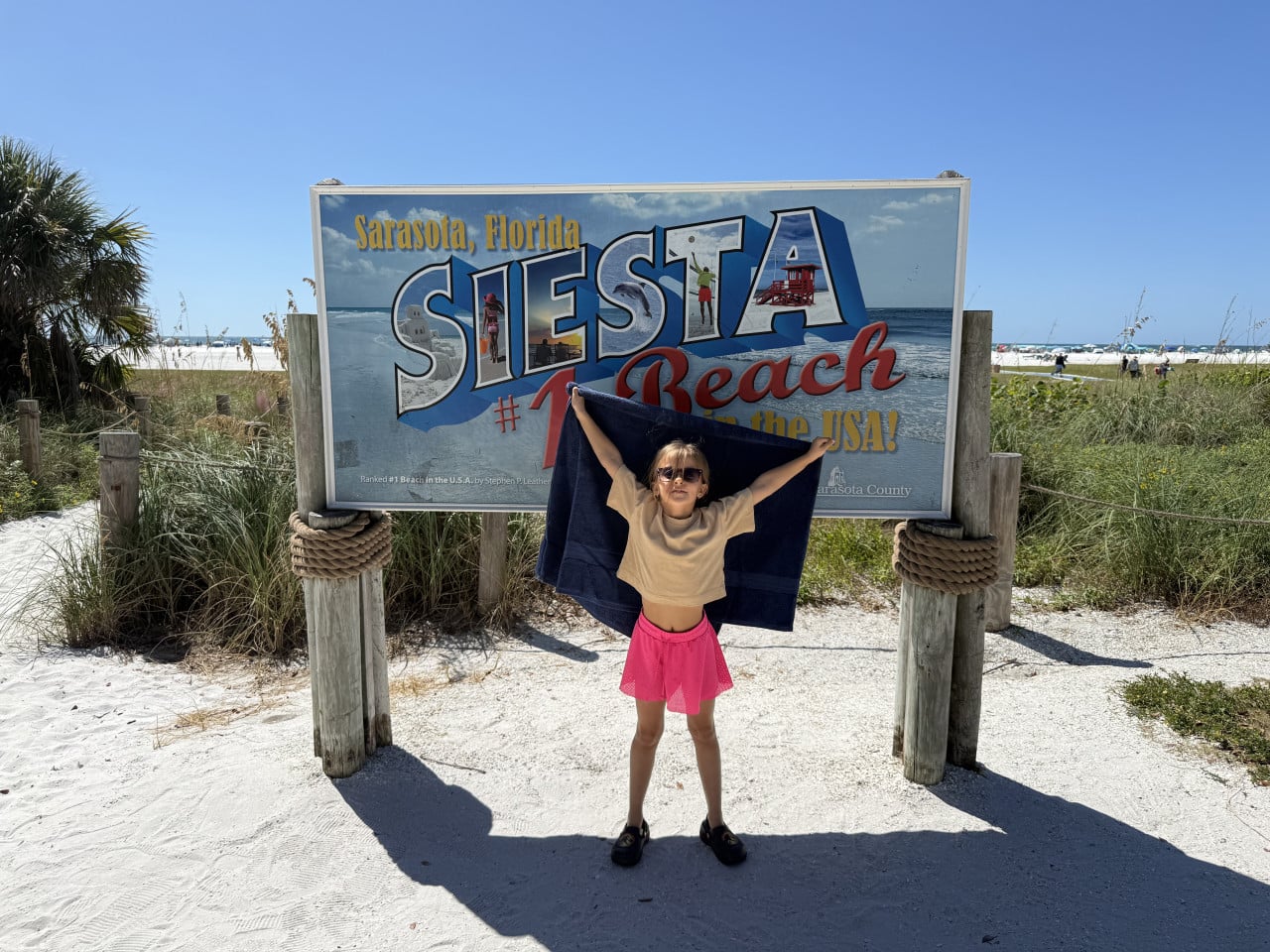 Dívka před cedulí Siesta Beach na slunečné pláži v Sarasotě, Florida.