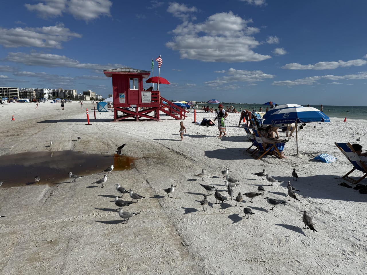 Siesta Key Beach s bílým pískem, červenou plavčíckou věží a lidmi u moře