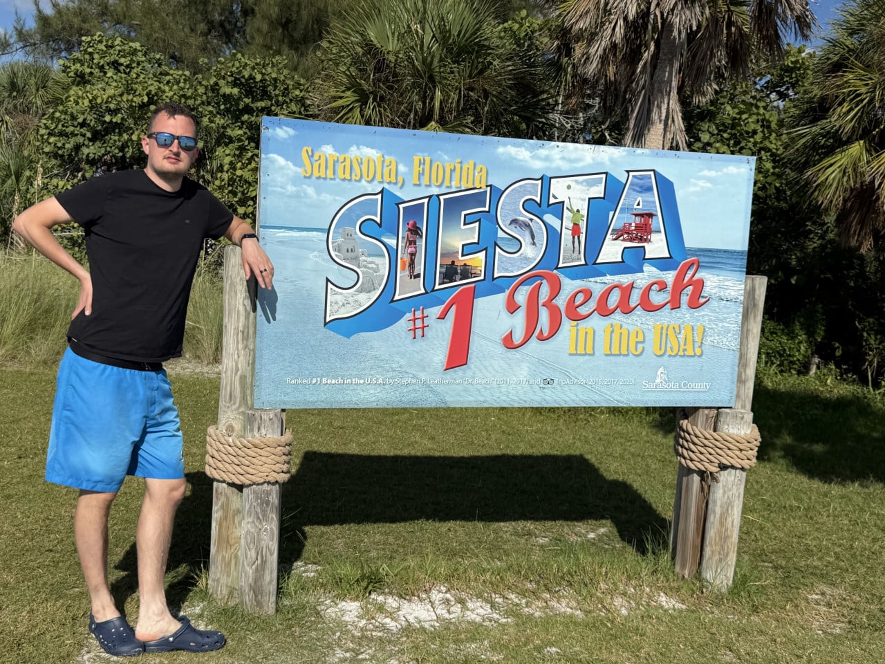 Muž stojí u cedule Siesta Beach #1 Beach in the USA v Sarasotě.