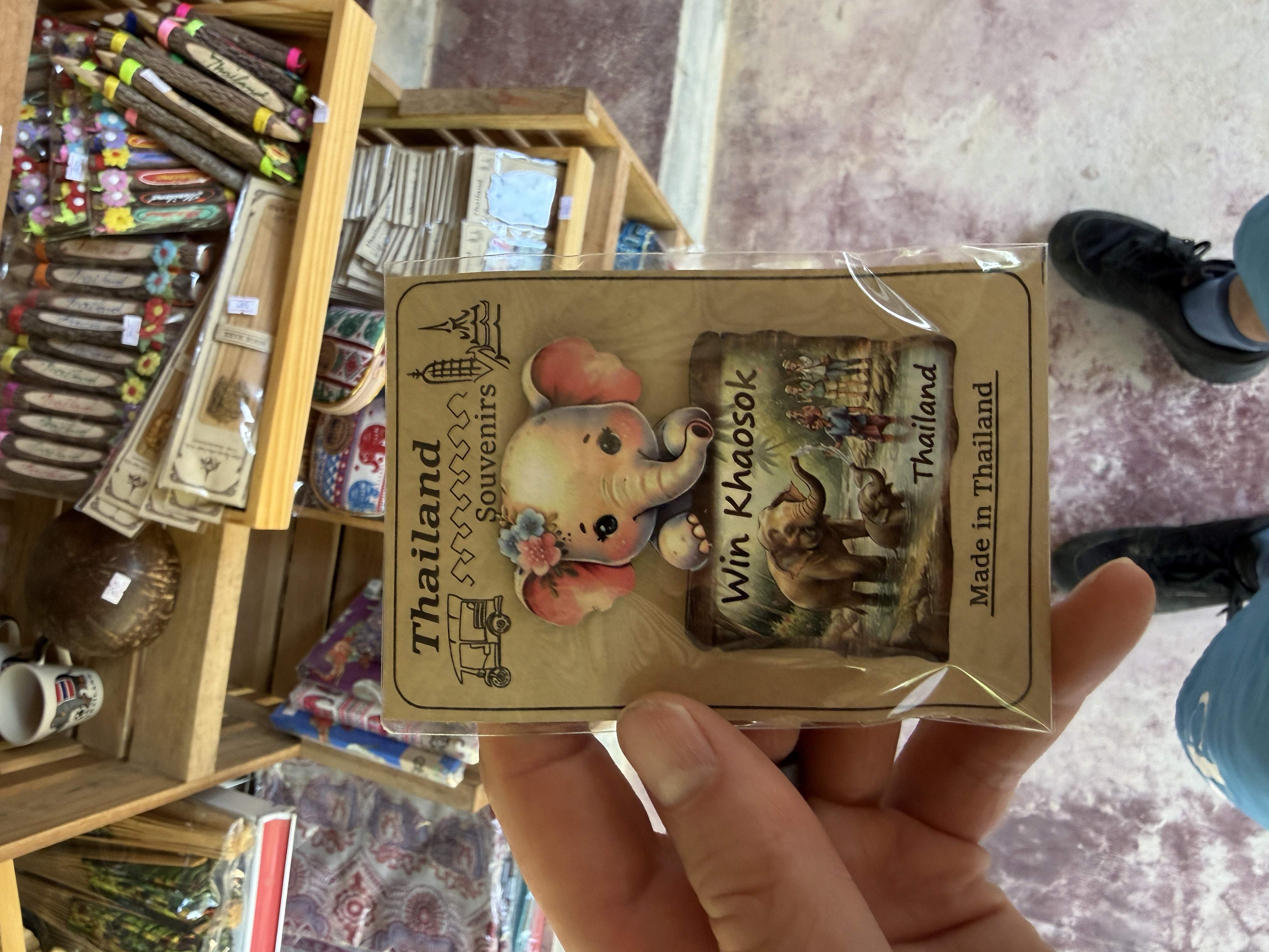 Ruka drží magnet se slonem, text Thailand Souvenirs, Win Khaosok, Made in Thailand