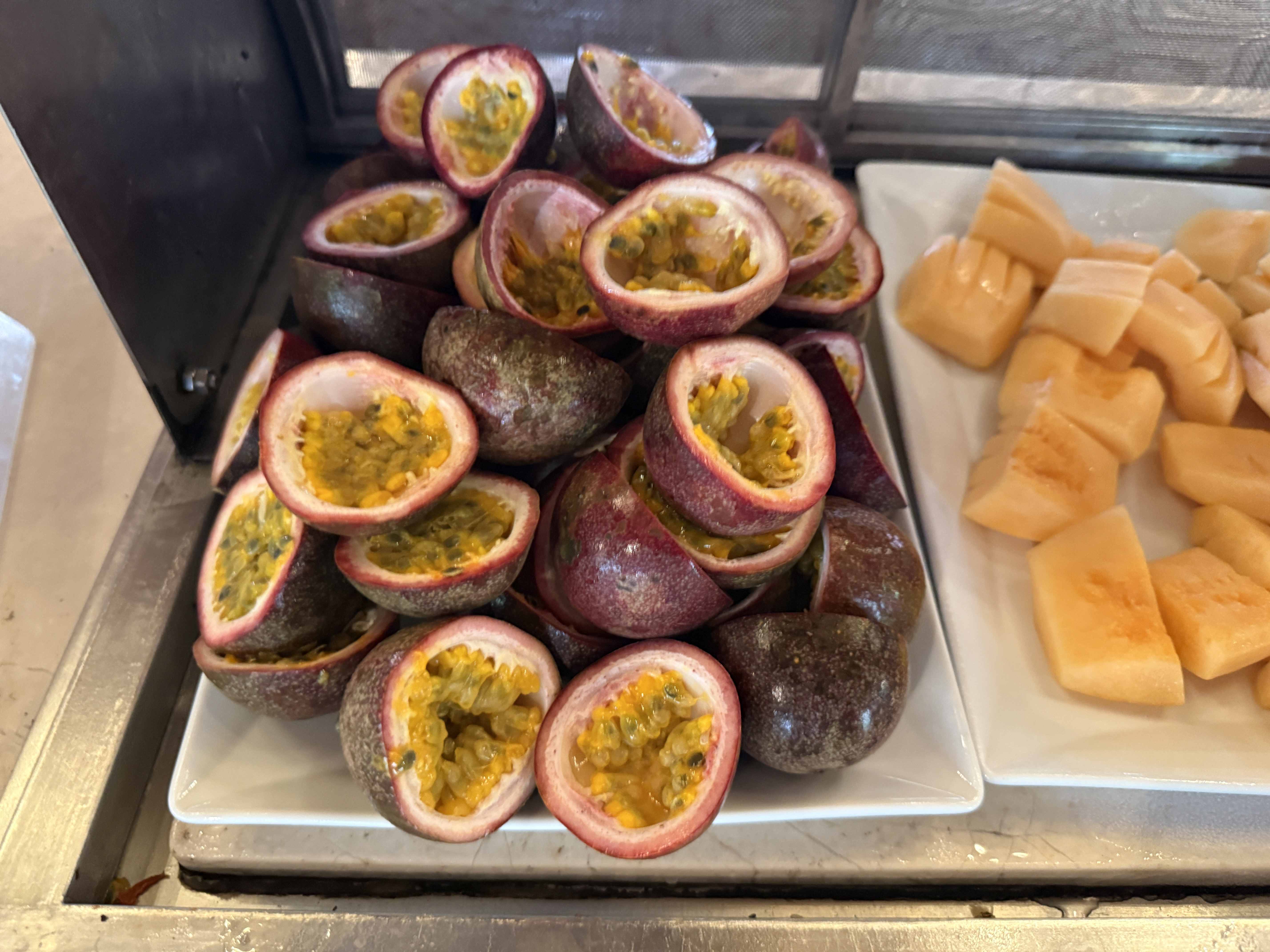 Mísa s rozpůlenými marakujami a vedle kousky melounu na talíři