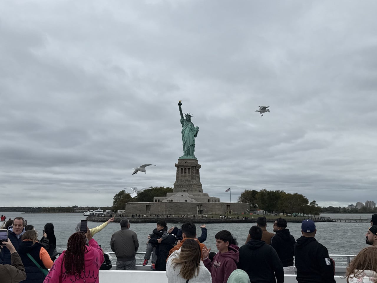 Socha Svobody na ostrově, pozorovaná z lodi s turisty v popředí.