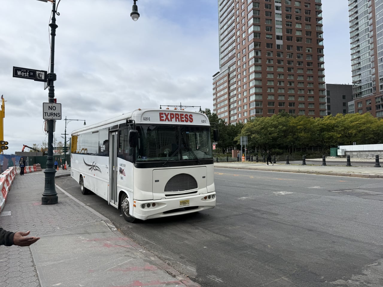 Bílý autobus EXPRESS u West St, vysoké domy a značka NO TURNS.