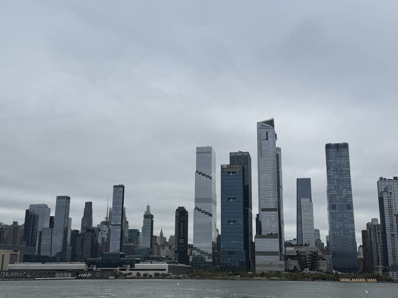 Panorama mrakodrapů Lower Manhattanu nad řekou pod zataženou oblohou
