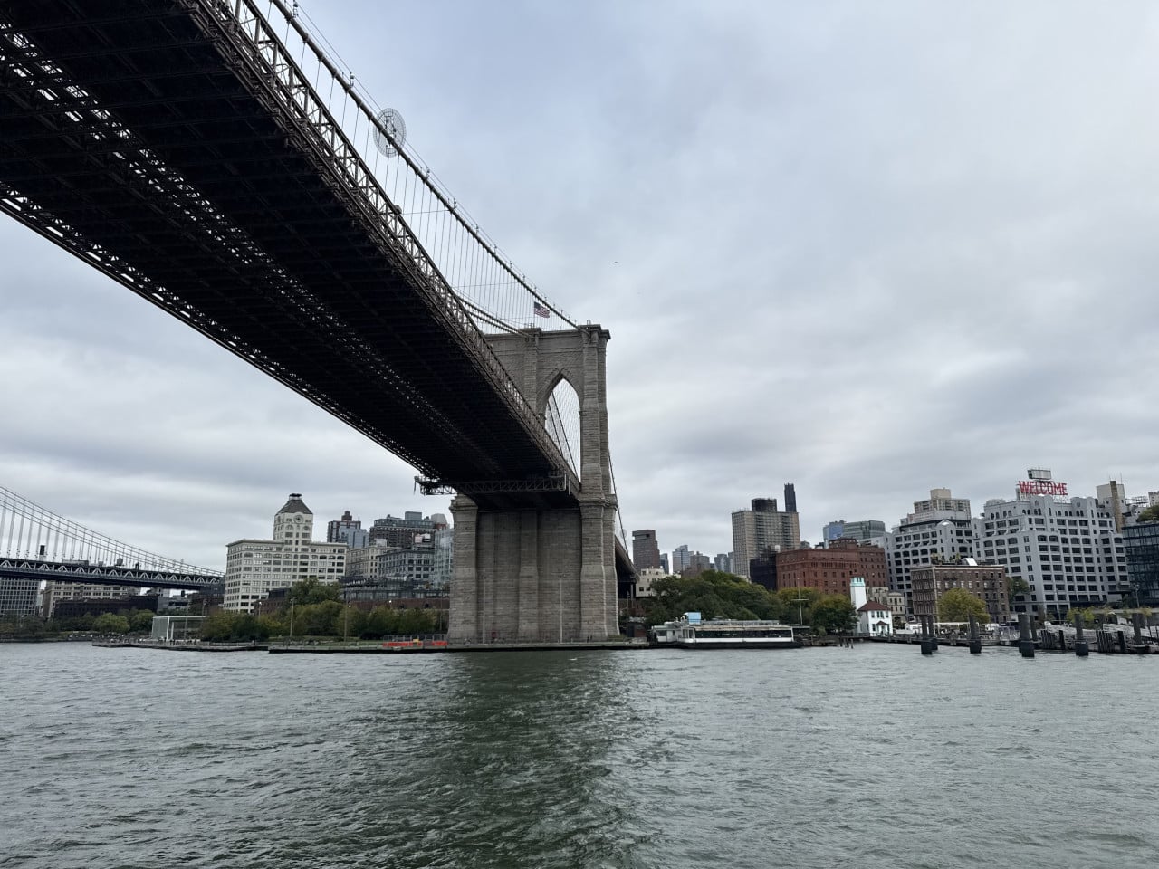 Brooklyn Bridge nad řekou s panoramatem Manhattanu a nápisem WELCOME.