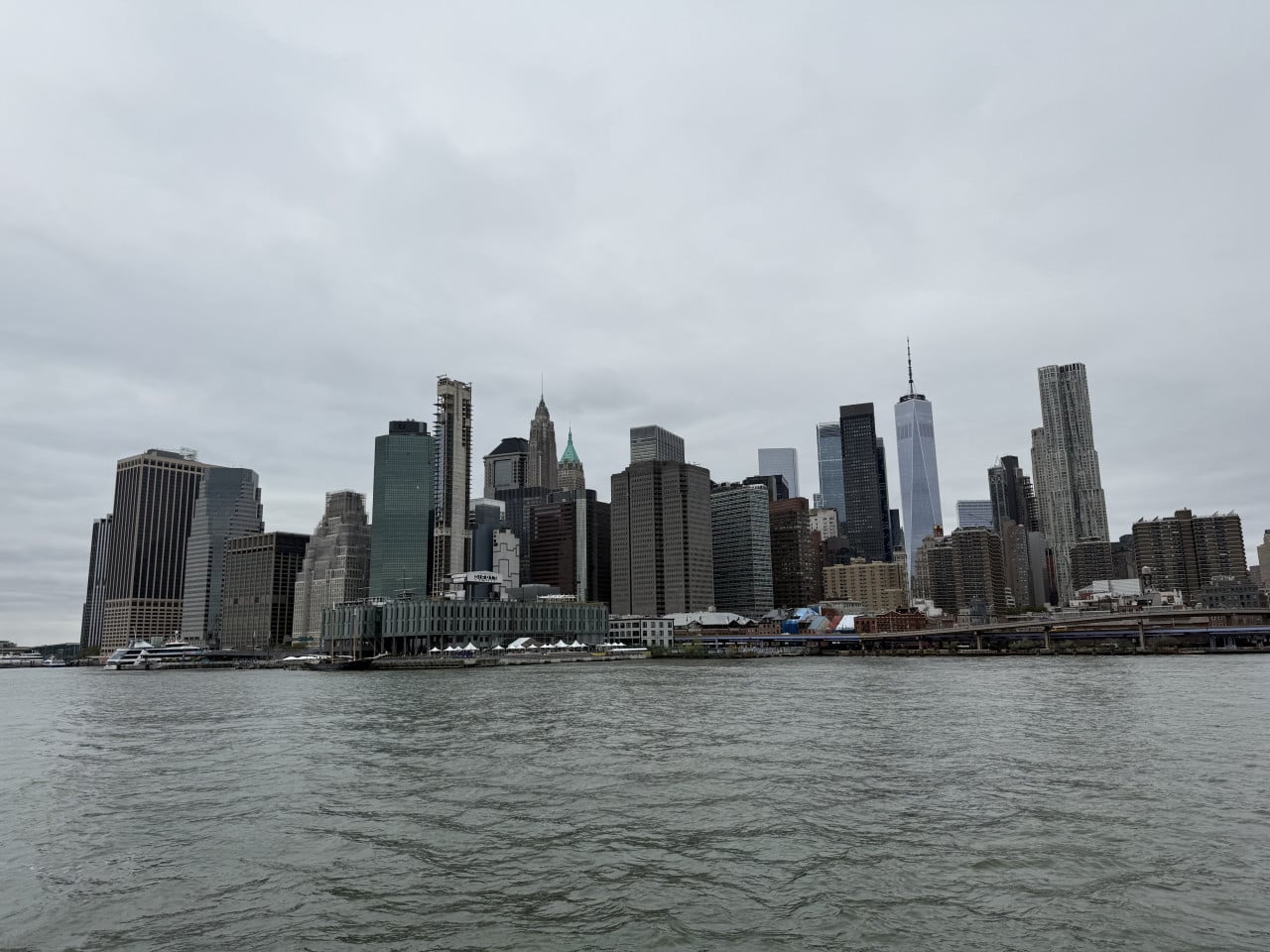 Panorama dolního Manhattanu přes řeku Hudson pod zamračenou oblohou.