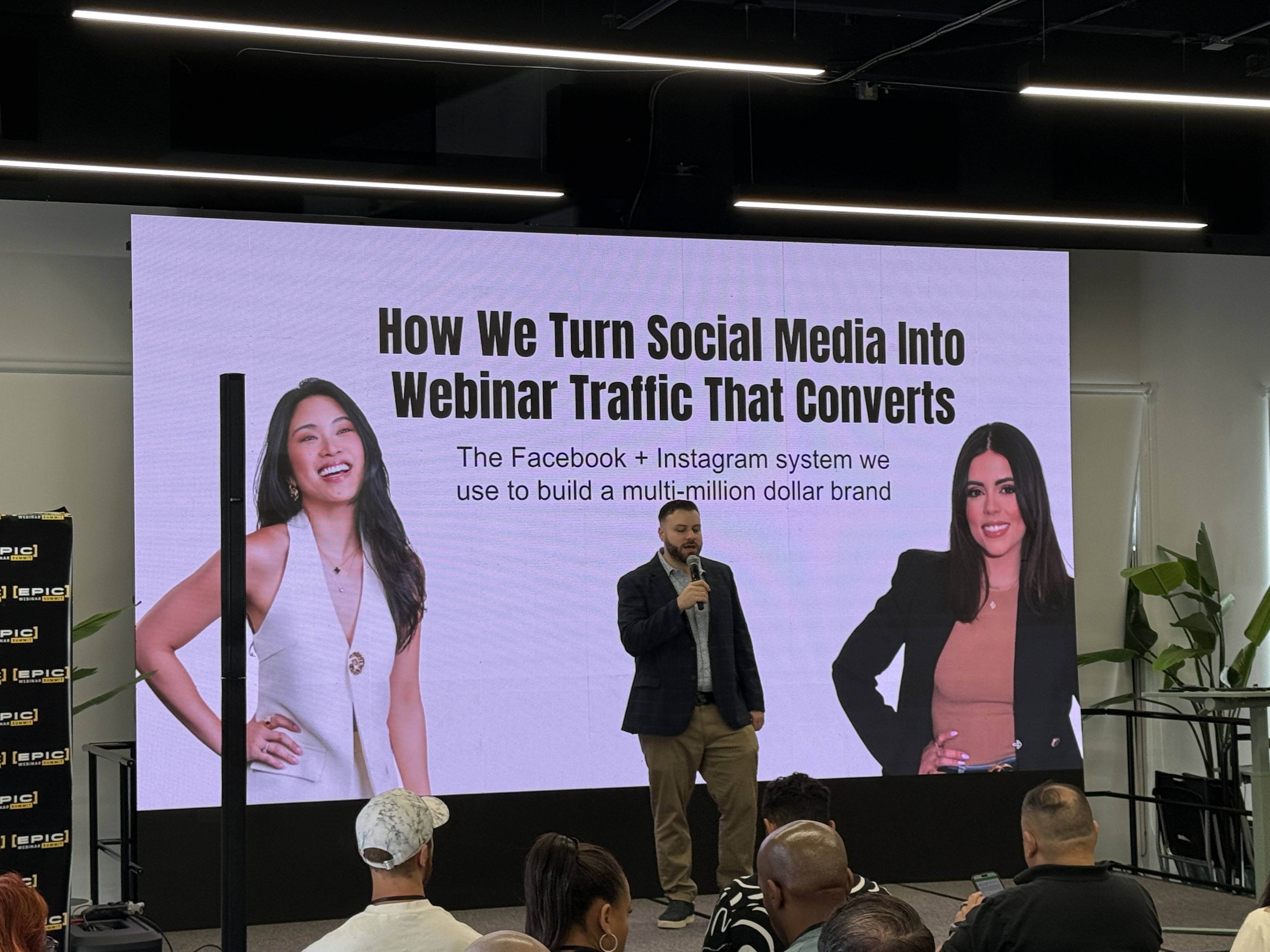 Přednášející s mikrofonem před plátnem How We Turn Social Media Into Webinar Traffic That Converts