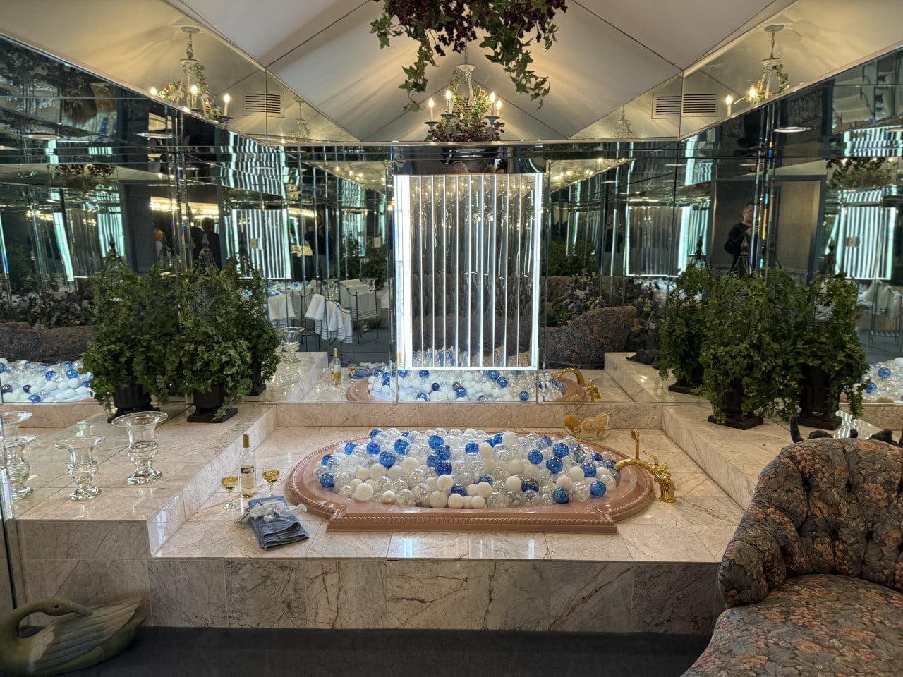 Zrcadlová koupelna se dvěma zapuštěnými vanami plnými modrobílých míčků, lustry a květinami.