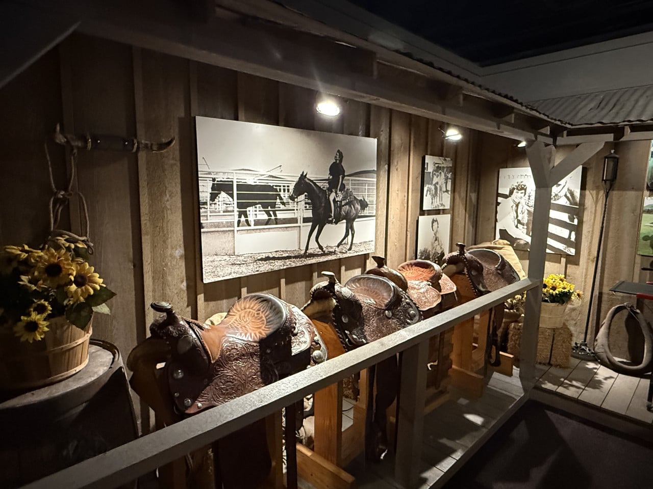 Sedla vystavená ve stodole, na stěně černobílé fotografie jezdce na koni