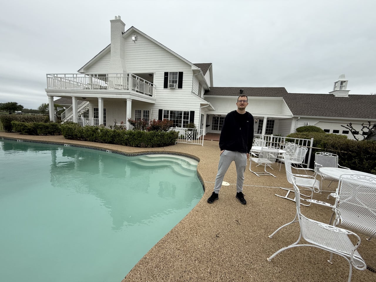 Muž stojí u bazénu před bílým domem Southfork Ranch, Texas