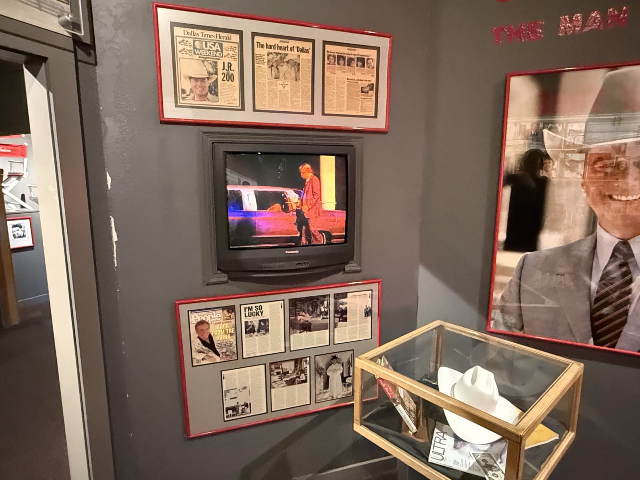 Expozice Southfork: TV s Dallasem, rámy Dallas Times Herald, vitrína s bílým kloboukem.