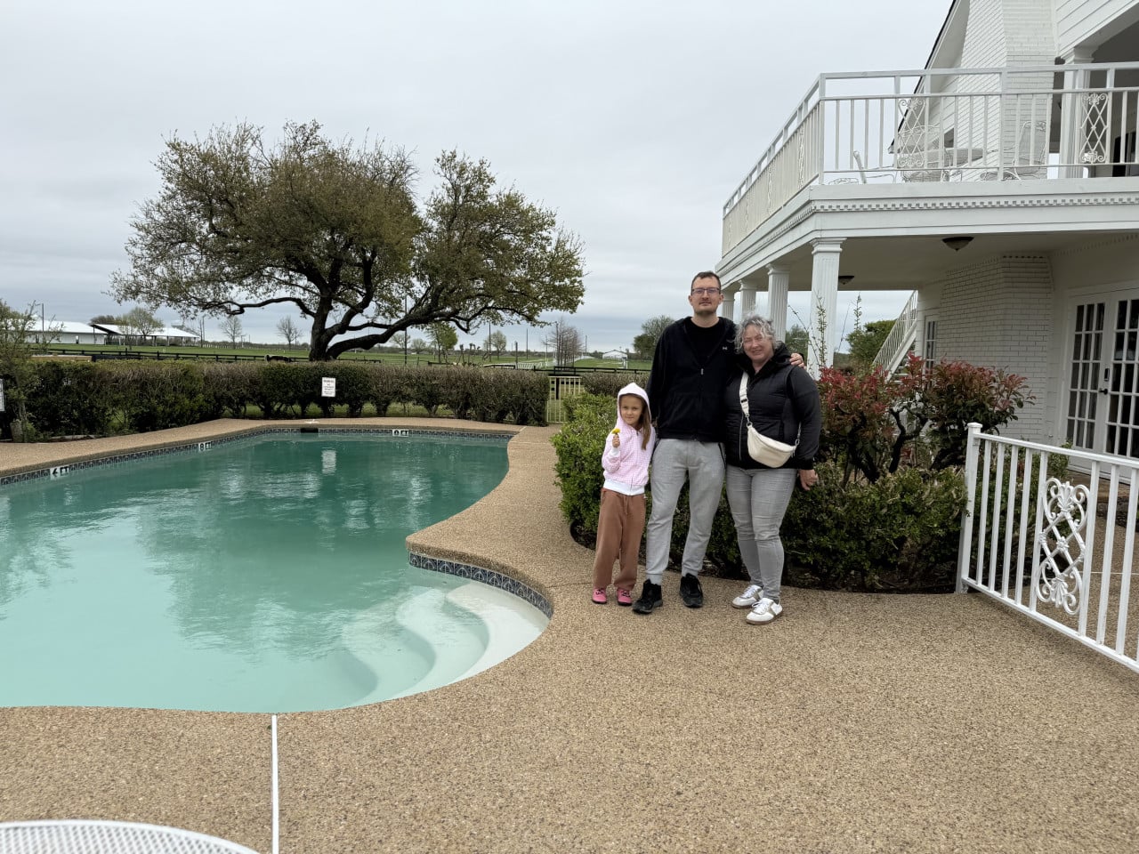 Tři návštěvníci pózují u venkovního bazénu vedle bílého domu Southfork Ranch.
