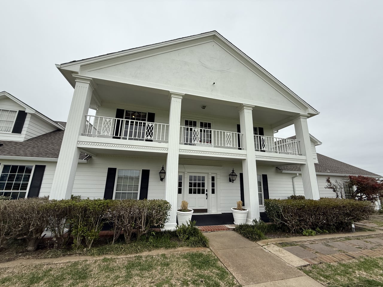 Bílá fasáda Southfork Ranch s vysokými sloupy, balkonem a hlavním vchodem.