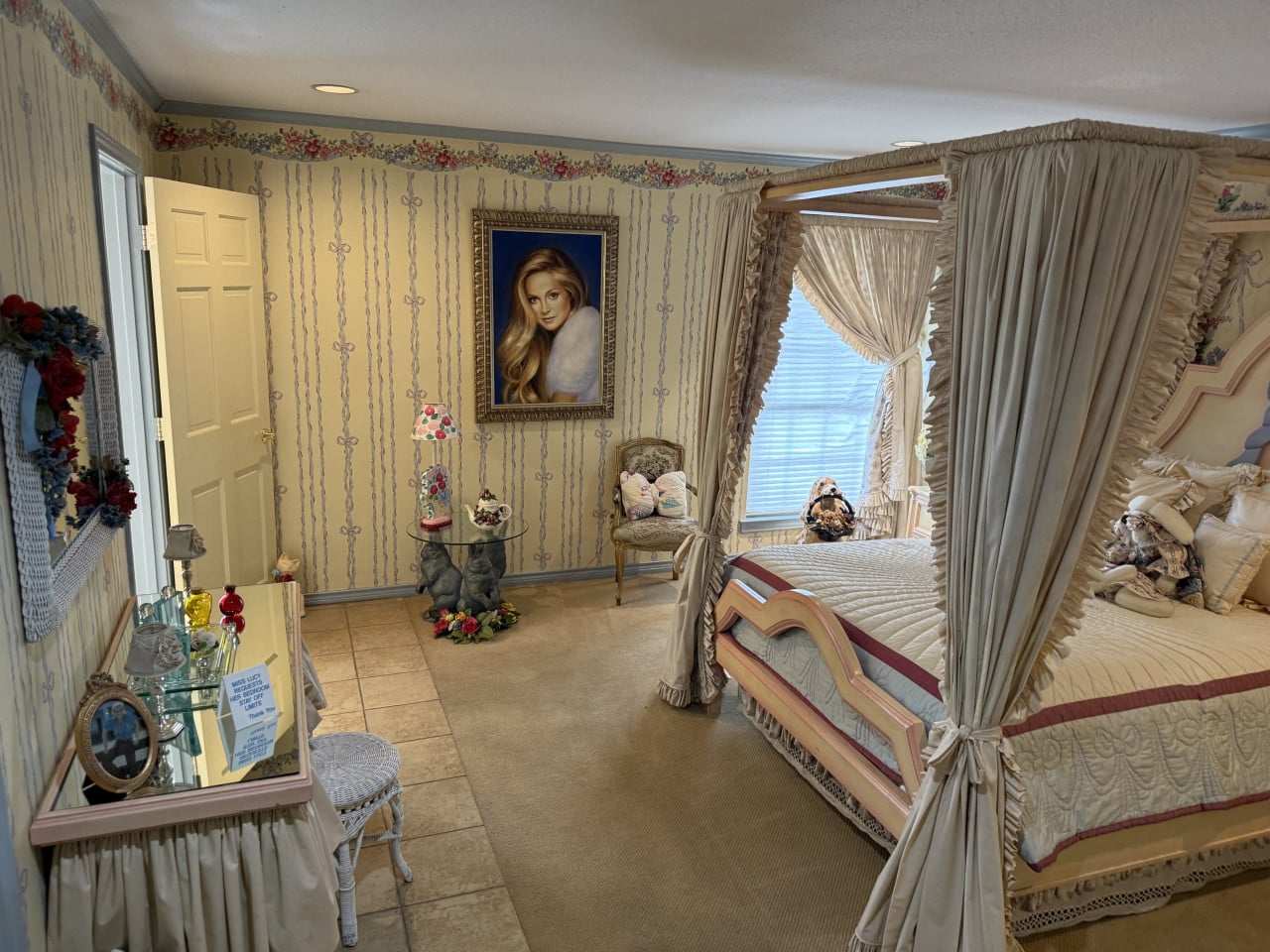 Ložnice s nebesy, portrét blondýny, toaletka a cedulka MISS LUCY STAY OFF.