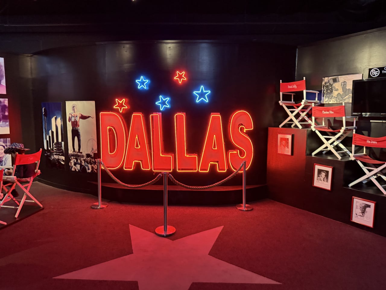 Neonový nápis DALLAS se svítícími hvězdami, červený koberec a režisérská křesla.