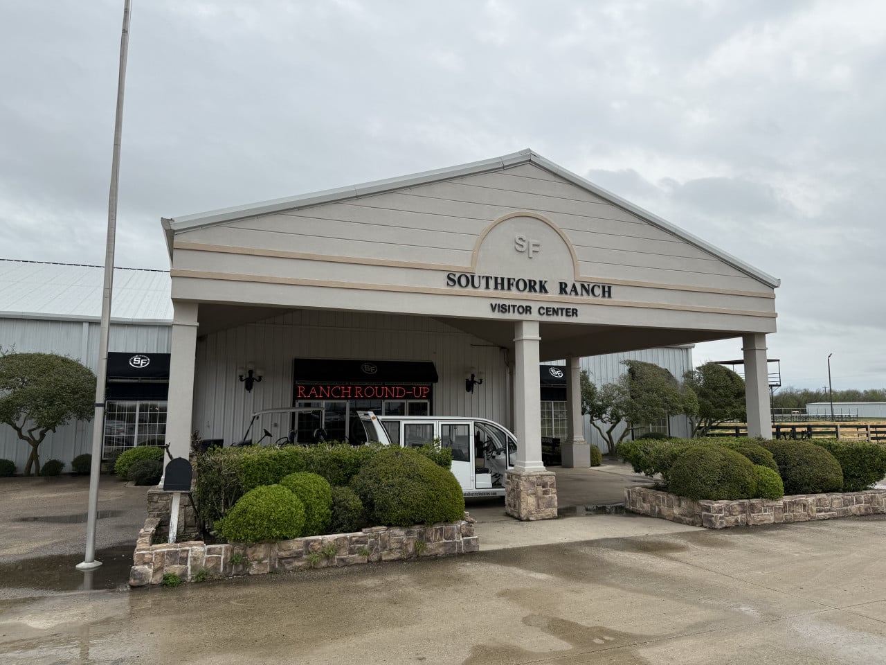 Vstup do SOUTHFORK RANCH VISITOR CENTER, nápis RANCH ROUND-UP a golfový vozík.