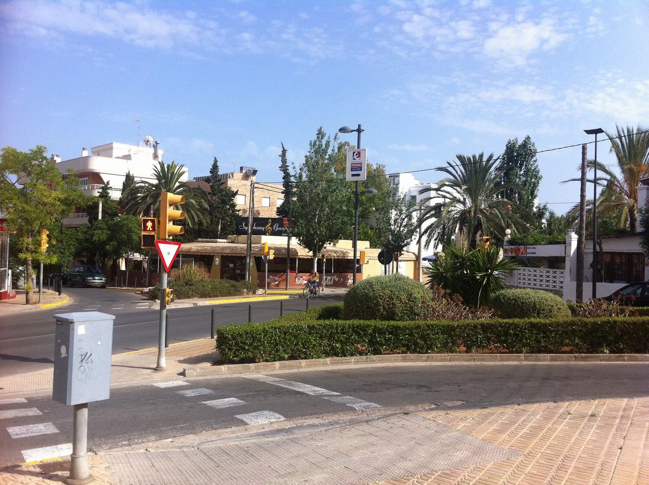 Křižovatka s palmami, semaforem a cyklistou; na sloupu značka EROSKI center.