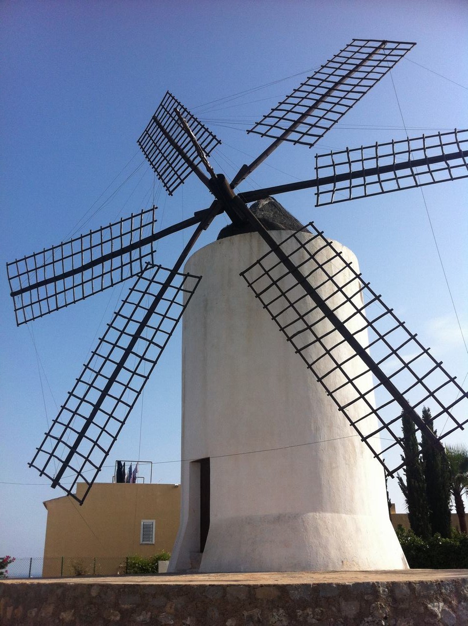 Bílý větrný mlýn s černými roštovými lopatkami proti modré obloze.