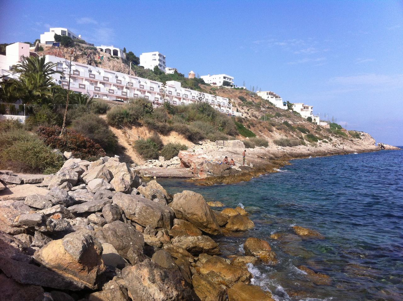 Skalnaté pobřeží s průzračným mořem, na svahu bílé domy a turisté