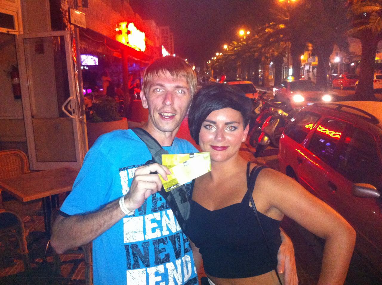 Muž a žena pózují v noci na ulici u neonového baru, drží lístky