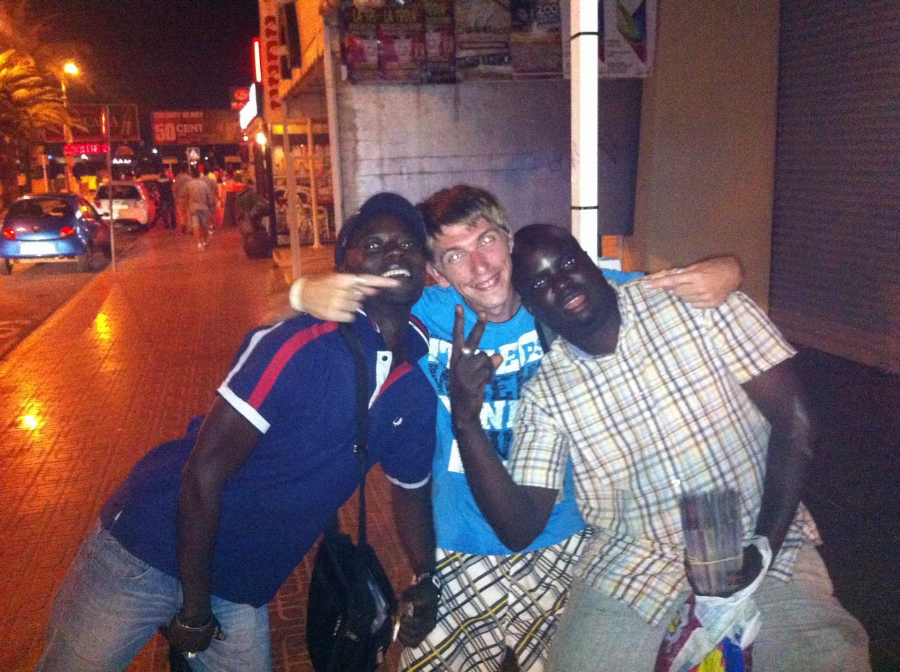 Tři muži se objímají na noční ulici, v pozadí nápis 50 CENT.