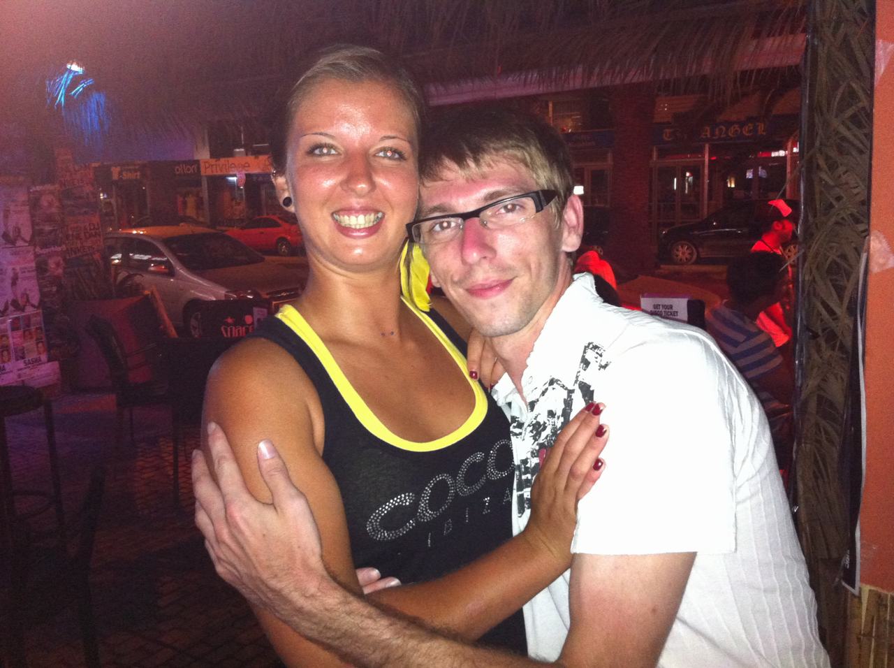 Usmívající se žena a muž objímající se v noci na ulici, nápis Cocoon.