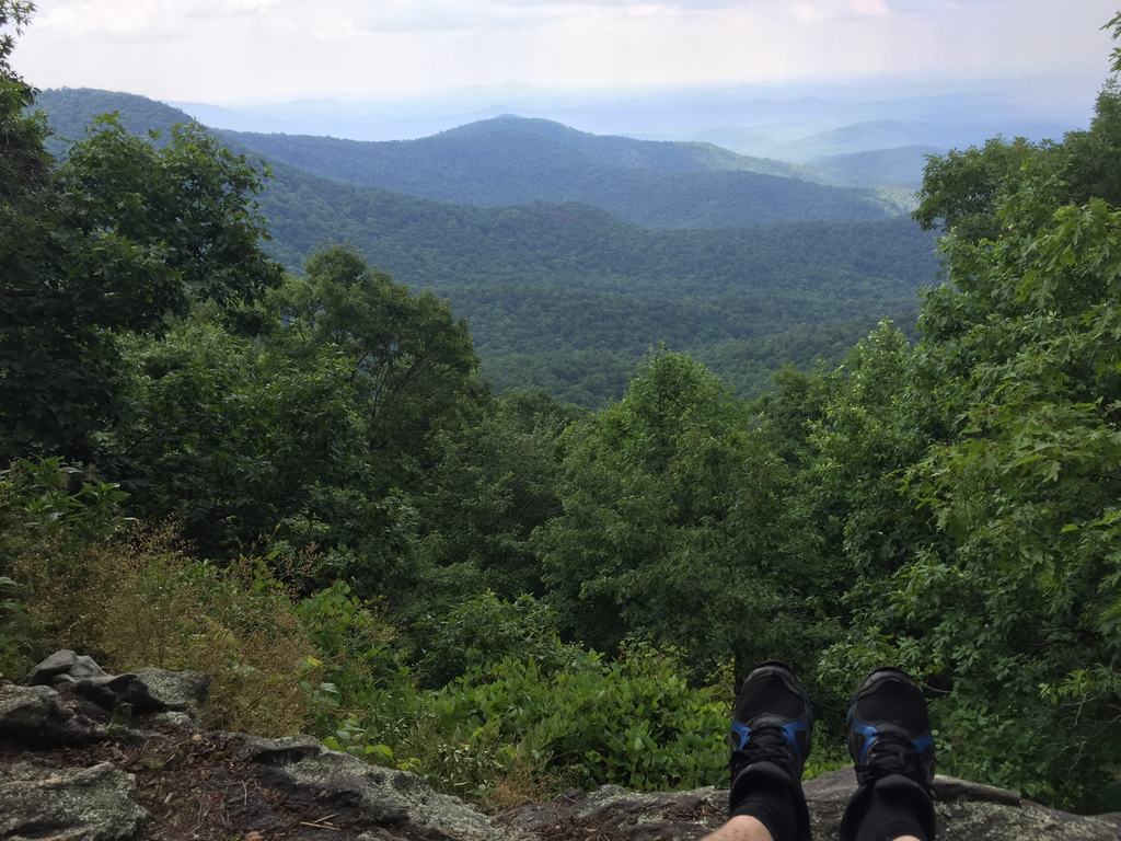 Výhled z útesu na zelené hory, v popředí turistické boty na skále